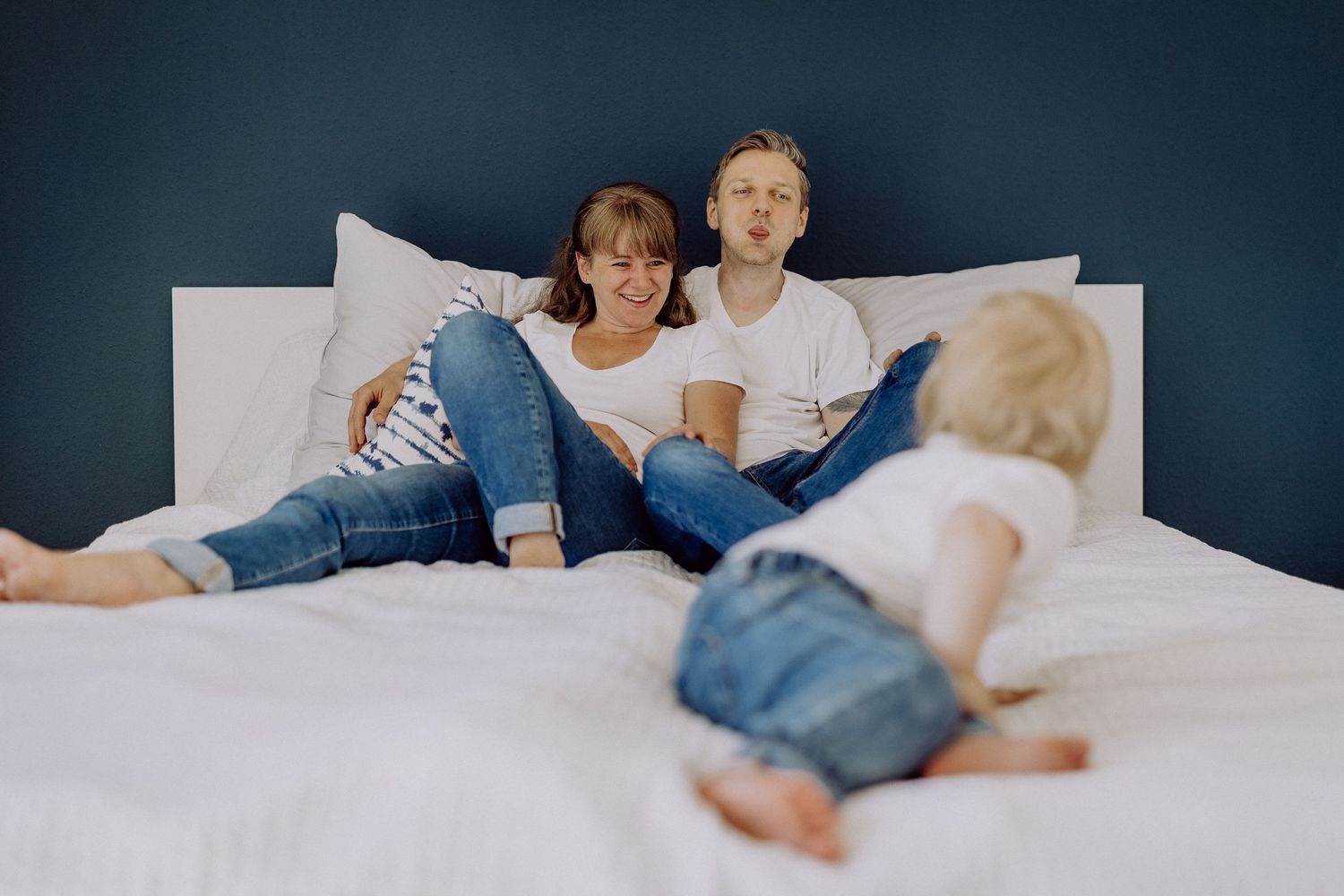 Familie entspannt sich gemeinsam auf einem weißen Bett in lässiger Jeanskleidung.