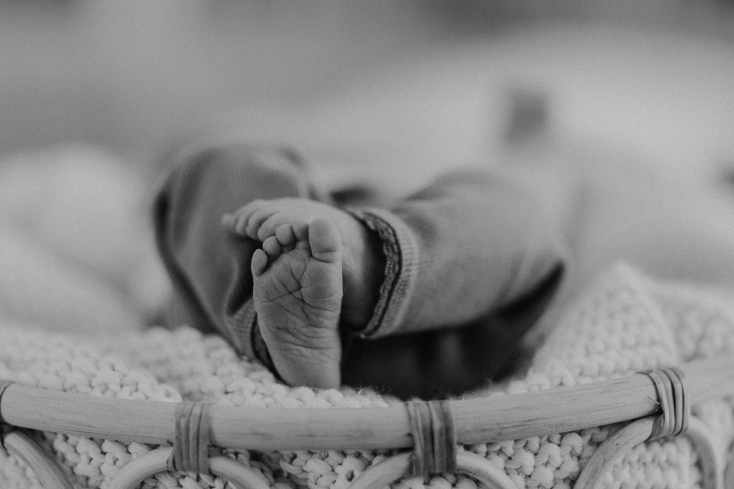 Schwarz-Weiß-Nahaufnahme des kleinen Fußes eines Babys auf strukturiertem Stoff.