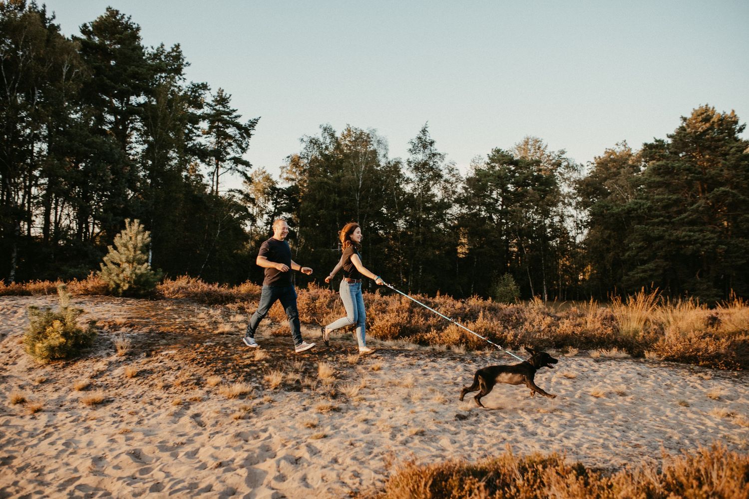 Paar, das während der goldenen Stunde mit seinem Hund einen Strandweg entlanggeht.