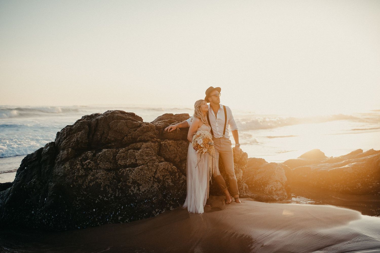 Paar umarmt sich auf Küstenfelsen während eines goldenen Sonnenuntergangs-Fotoshootings.