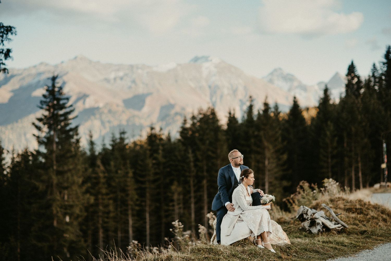 Hochzeitspaar steht vor Bergkulisse mit immergrünem Wald darunter in Österreich.