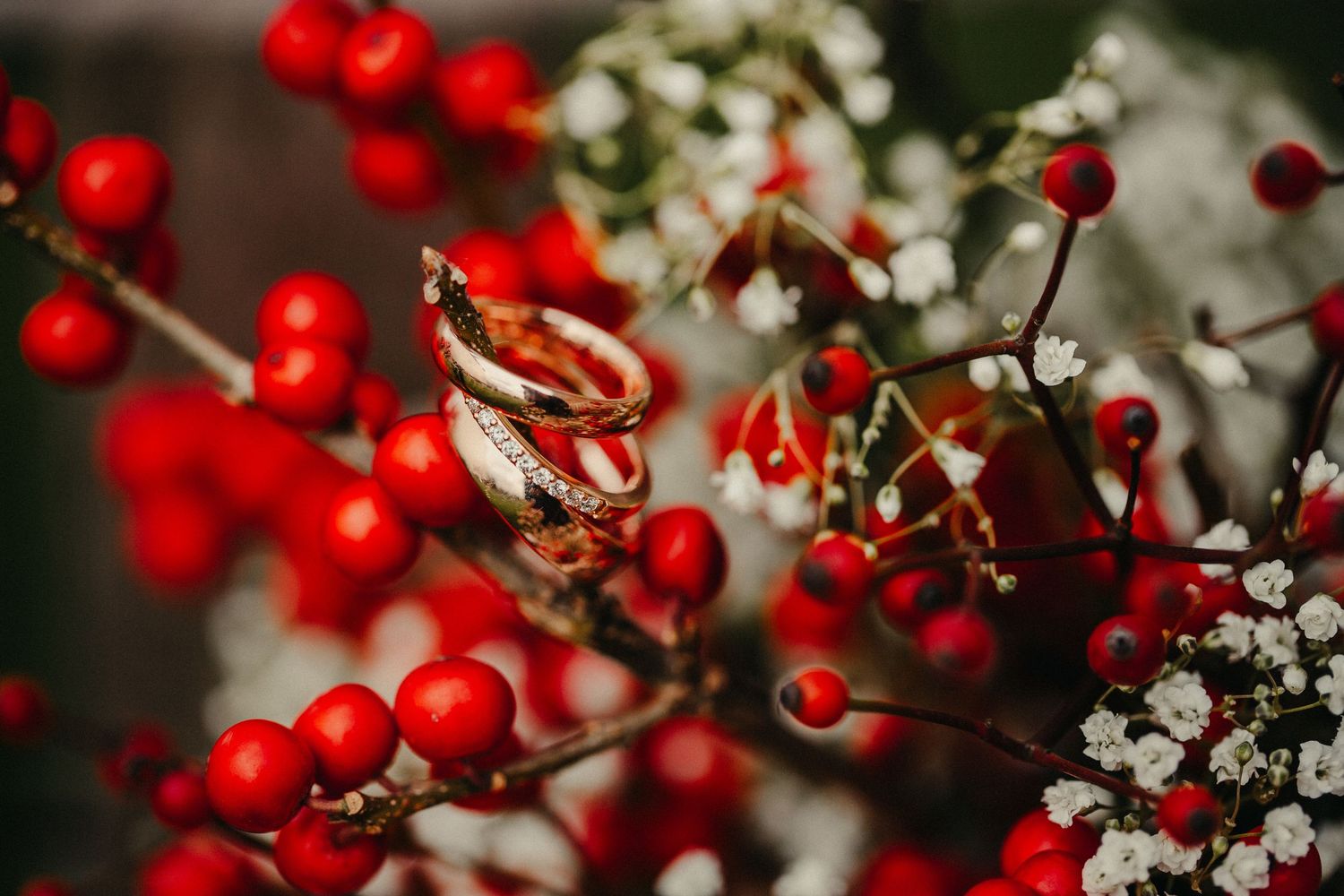 Eheringe kunstvoll fotografiert mit roten Beeren und weißen Blumen in Makrodetails.