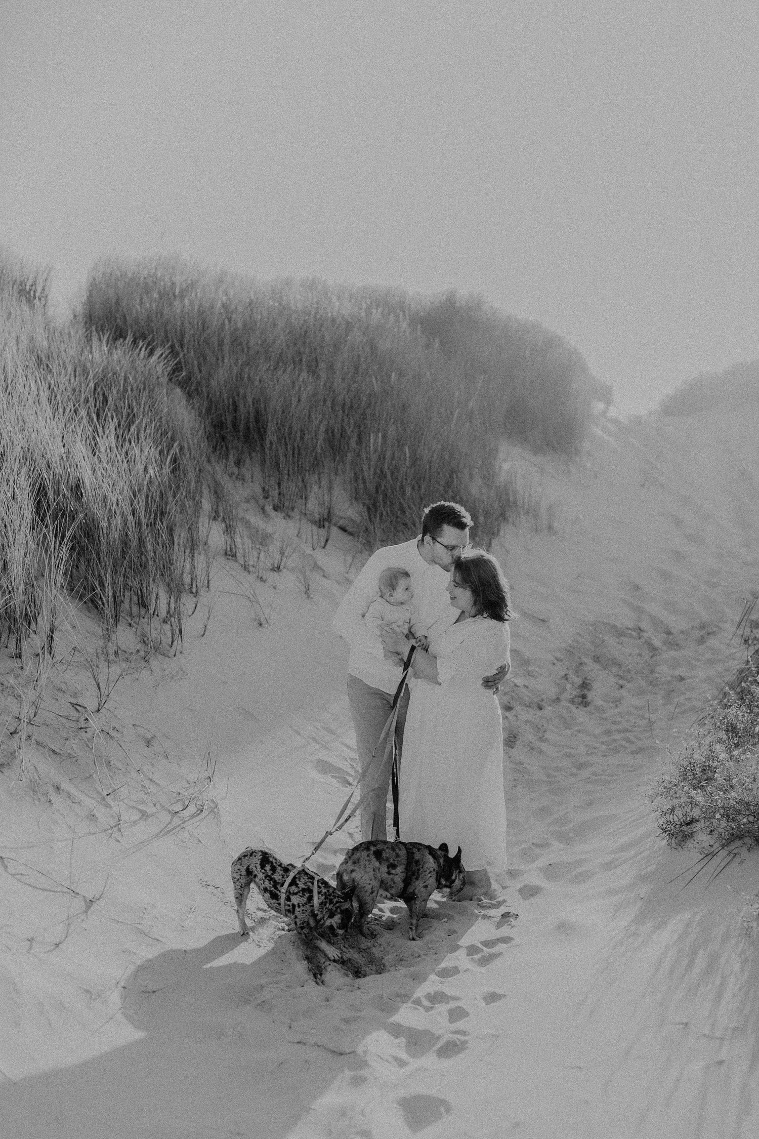 Paar geht mit ihren Hunden auf Sanddünen in einer romantischen schwarz-weißen Strandszene spazieren in Sankt Peter Ording.