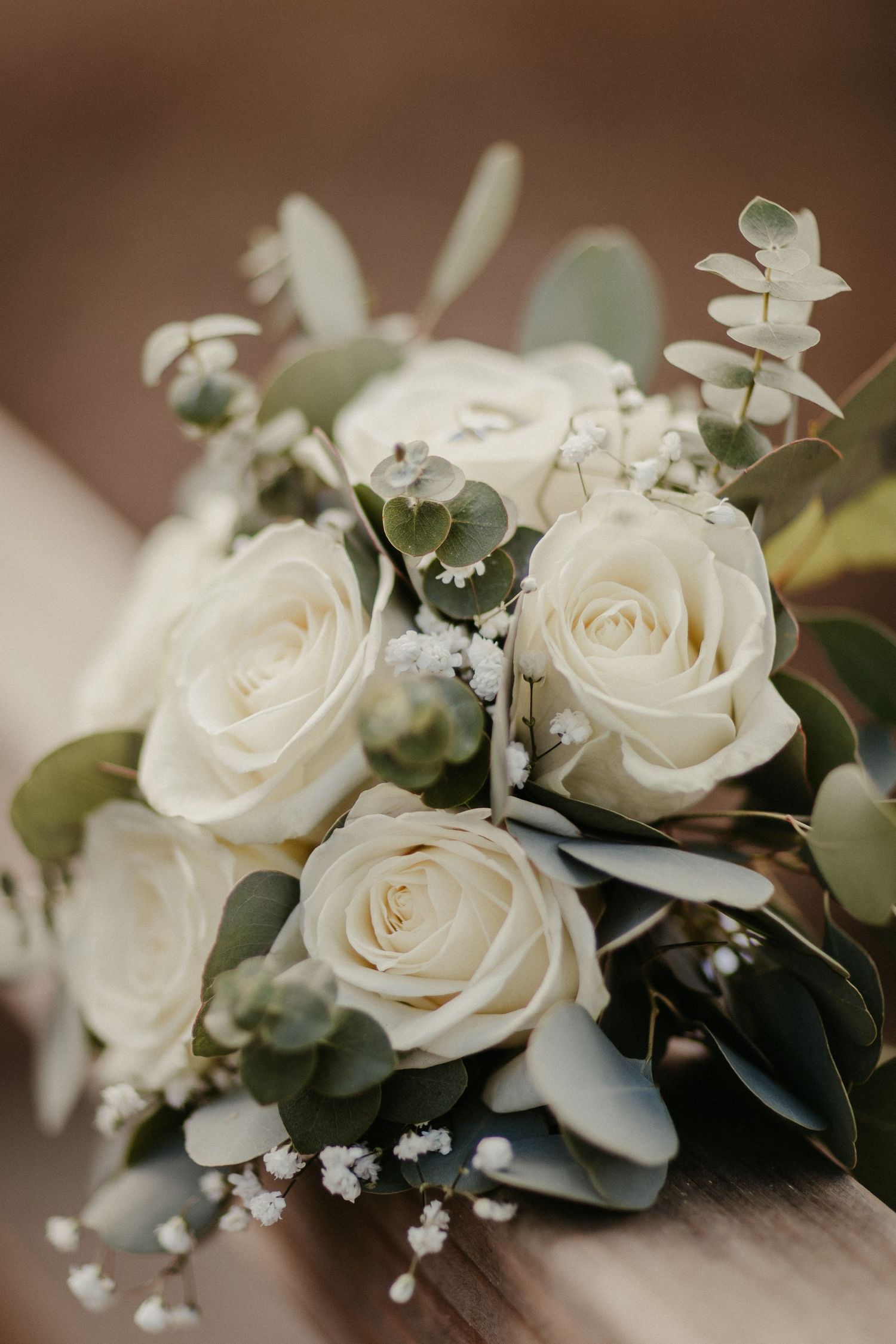 Weiße Rosen und Eukalyptusblätter in einem eleganten Brautstrauß angeordnet.