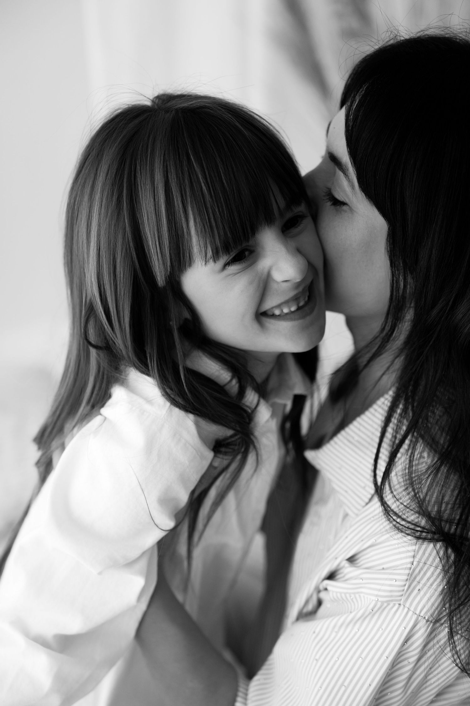 Black and white photo of mother whispering to smiling young daughter.