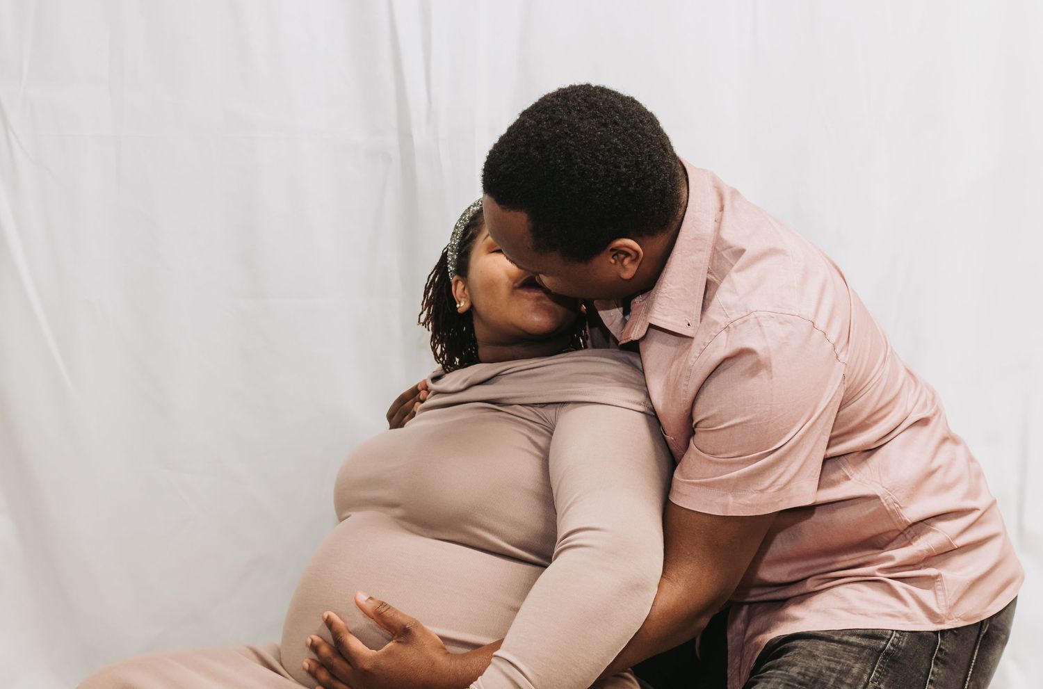 A loving couple shares an intimate moment during a maternity photoshoot against a white backdrop.