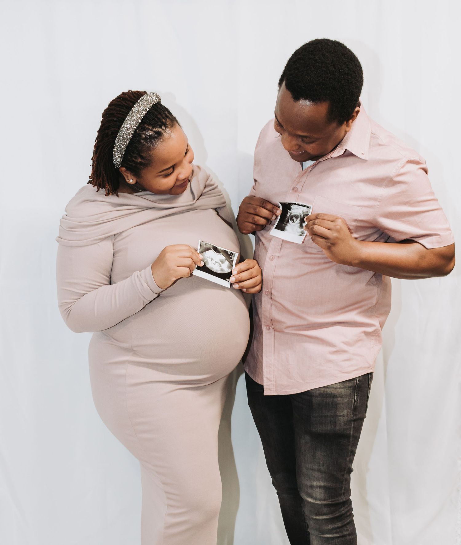 Expectant couple shares a tender moment looking at ultrasound photos while wearing matching pink outfits.
