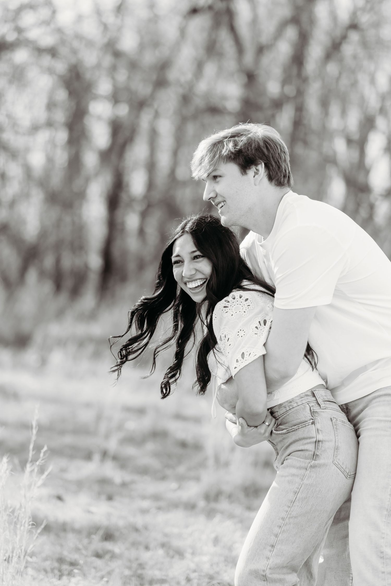 Black and white romantic engagement photos show a couple sharing joyful moments in a dreamy outdoor forest setting.
