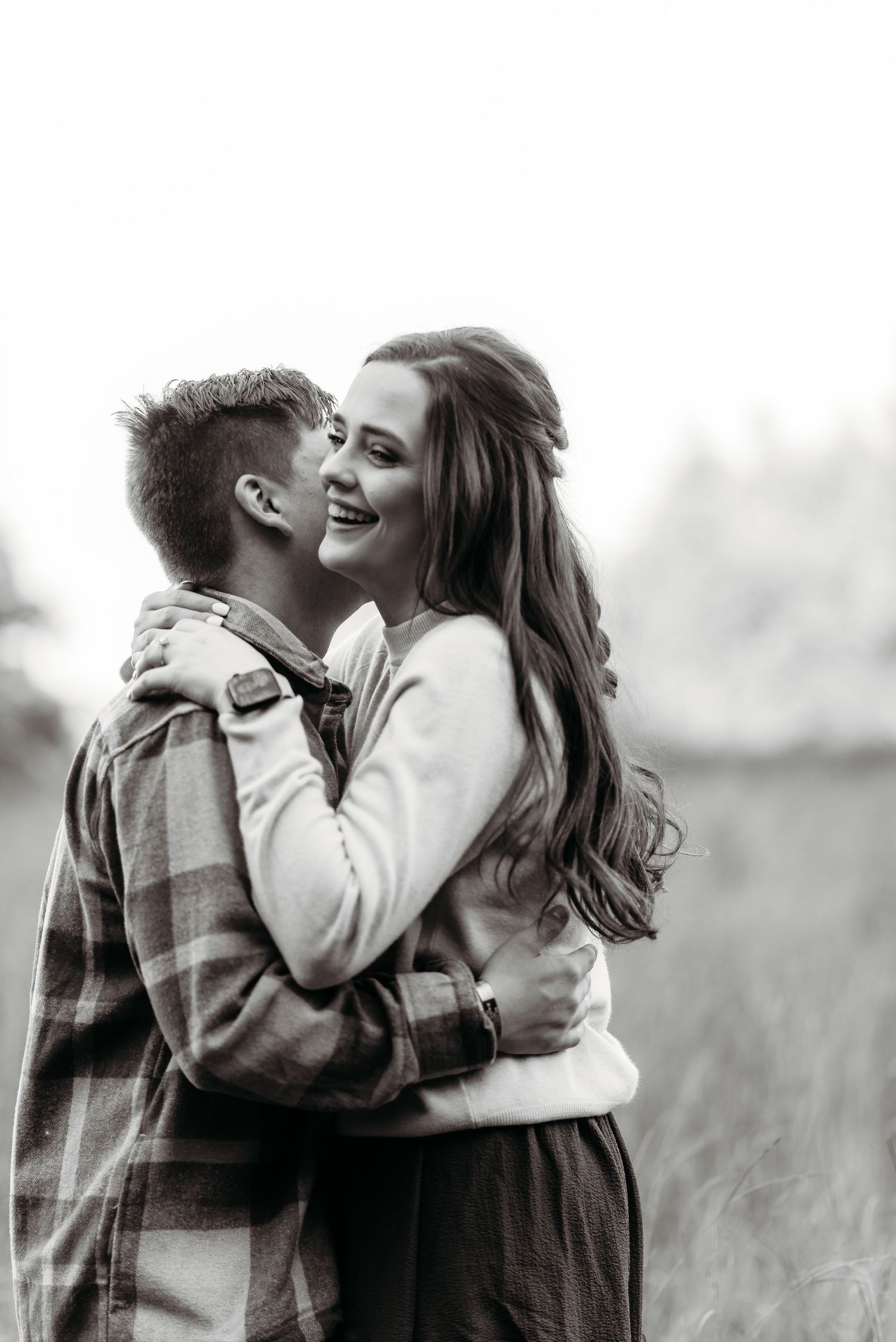 A romantic black and white portrait of a couple embracing in a field.