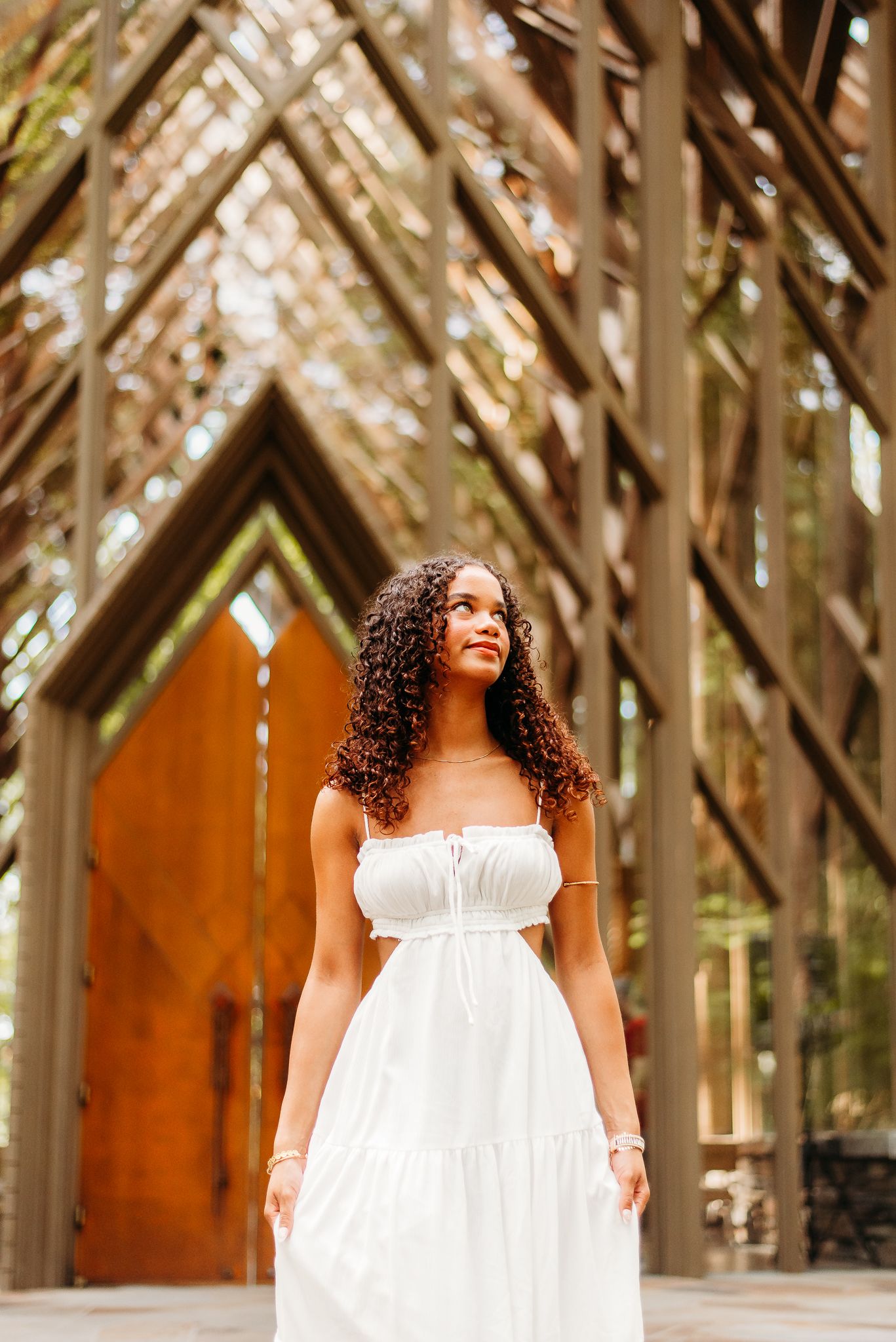 Woman in white dress poses elegantly in front of wooden chapel architecture.