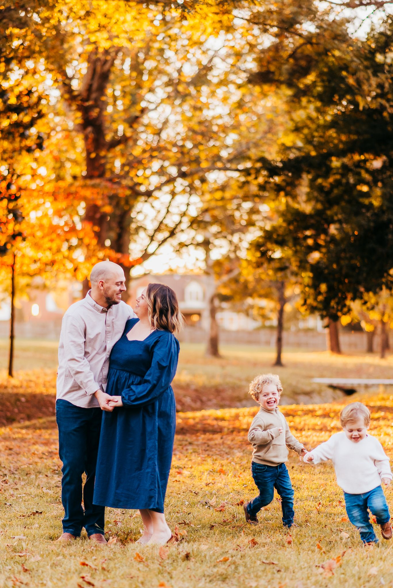 Family enjoying autumn scenery as young children play in background during outdoor photo session.