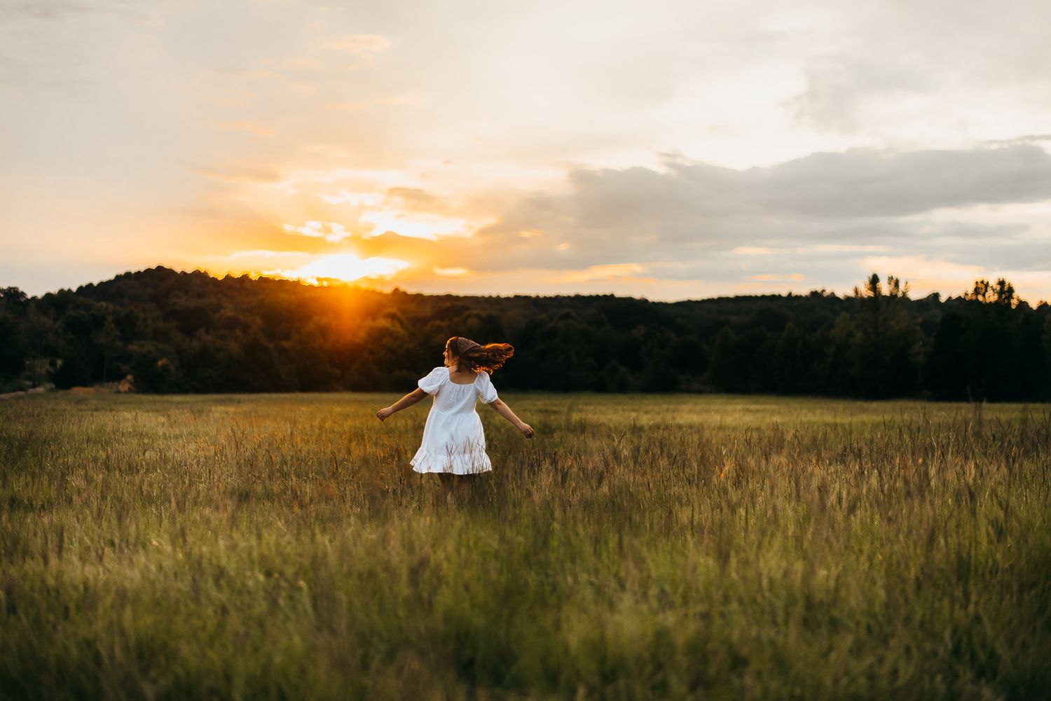 Silhouette in flowing dress spinning in golden wheat field at sunset.