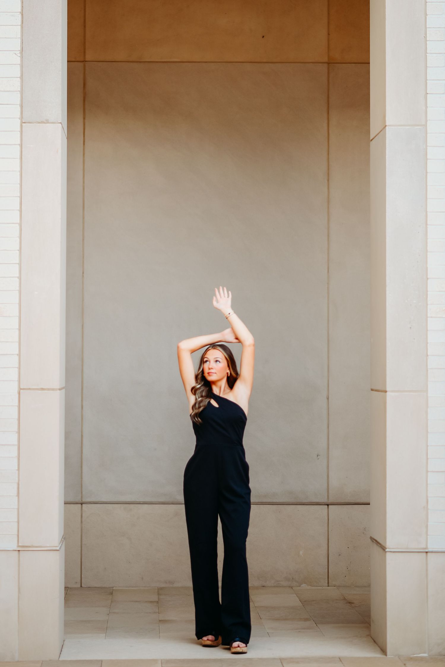 A person in a black jumpsuit poses with raised arms in an architectural doorway.