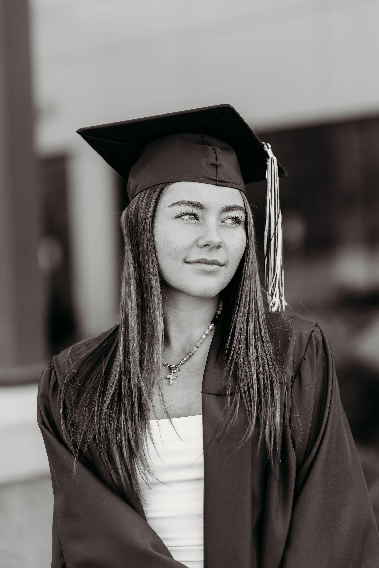 Black and white graduation portrait showing graduate in cap and gown with tassel looking thoughtfully to the side.
