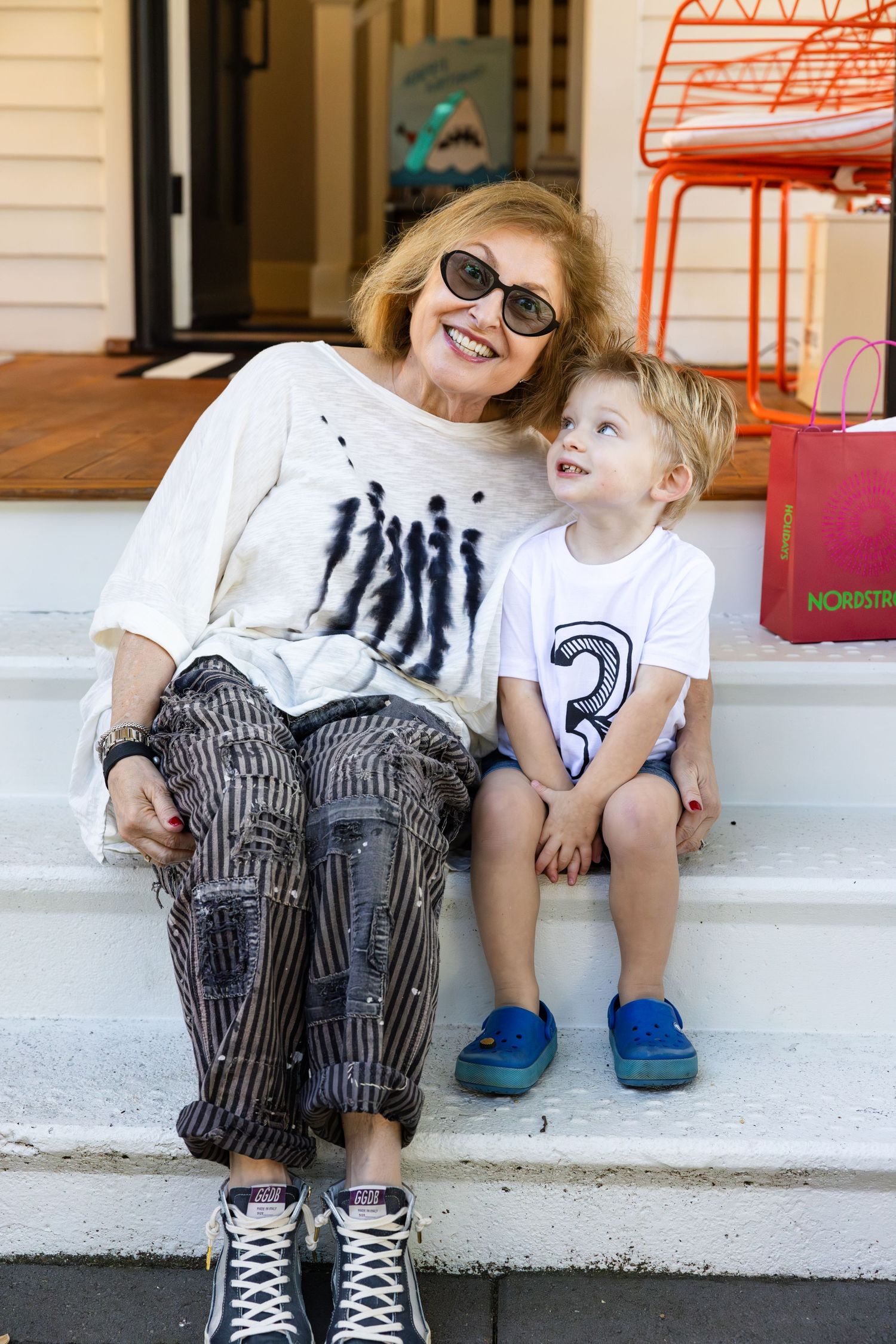 A joyful pair sitting together on white front steps, wearing casual t-shirts and fun patterned pants.