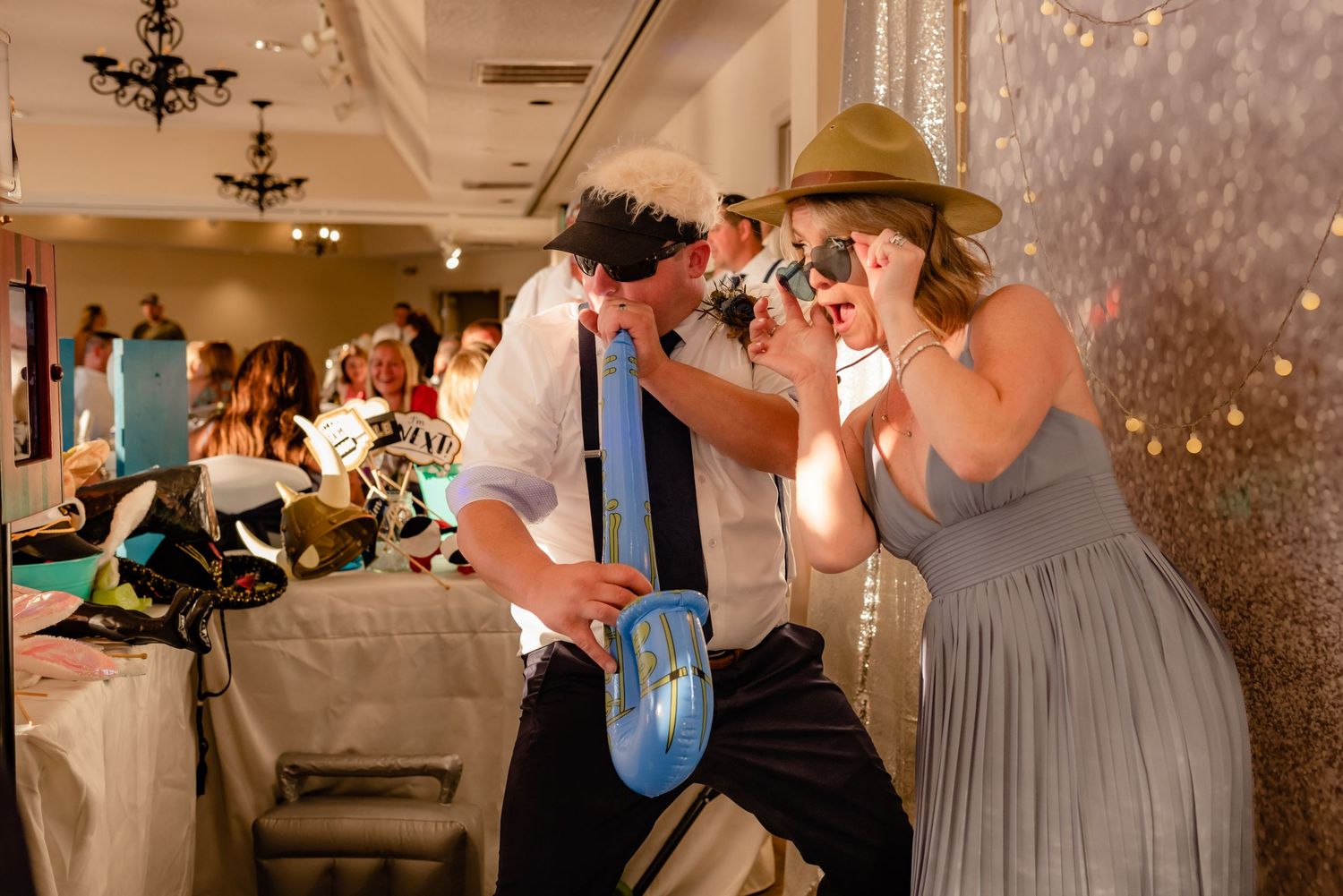 Wedding guests dancing and celebrating on a dance floor during an indoor reception with sparkling decor and lighting.