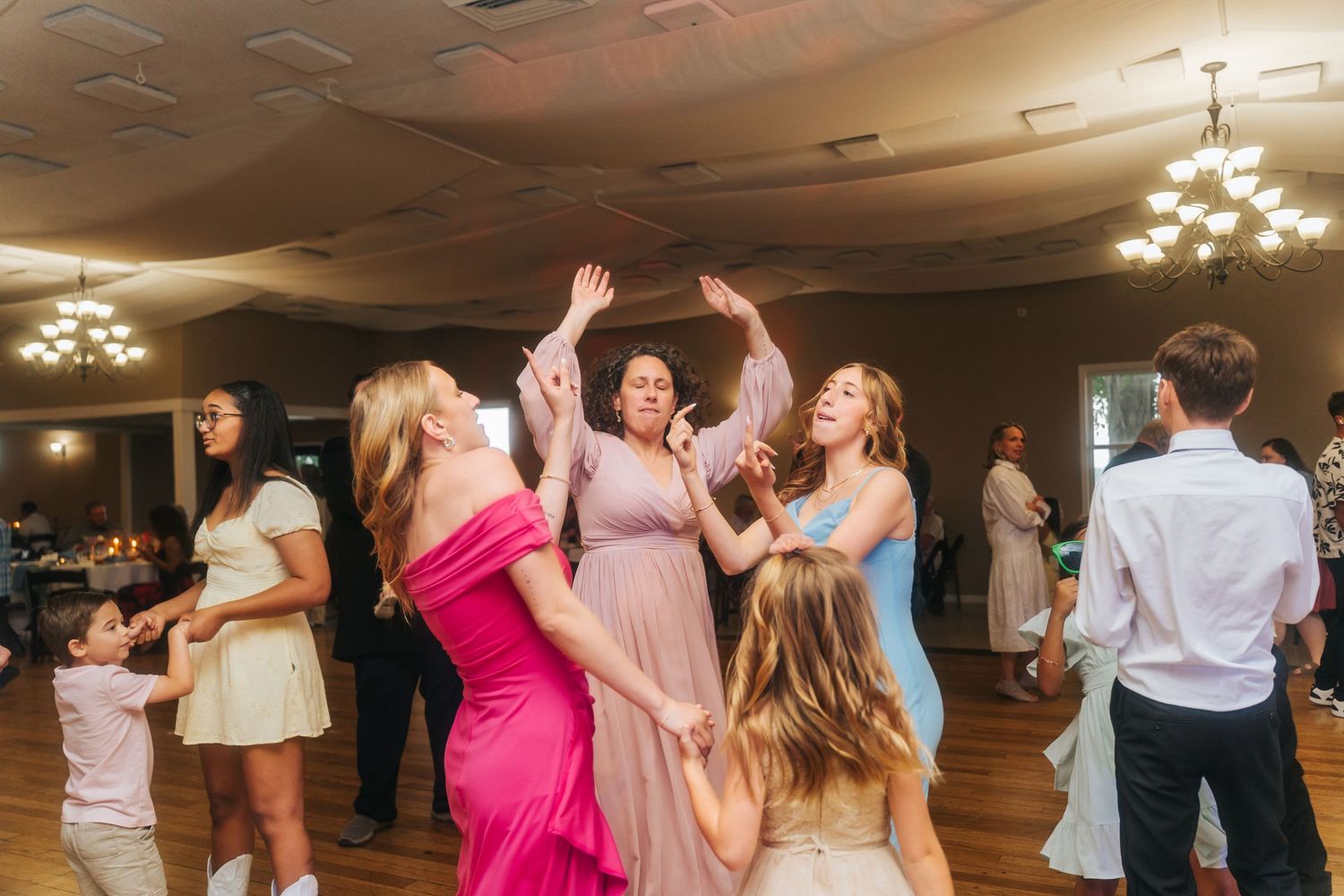 Wedding guests dance together on a dimly lit dance floor during an evening reception celebration.