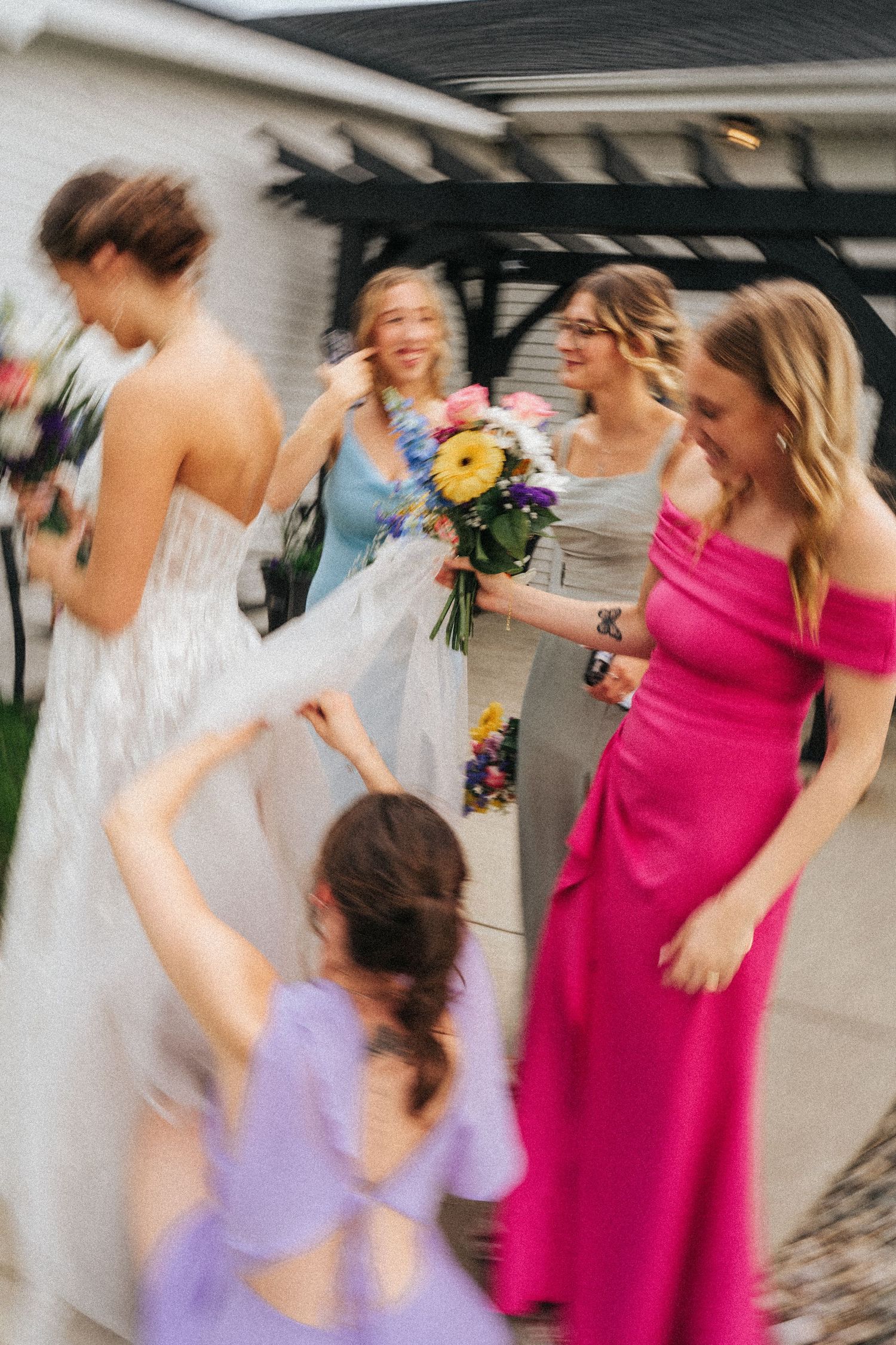 A blurry candid moment of bridesmaids in colorful dresses laughing and celebrating at a wedding.