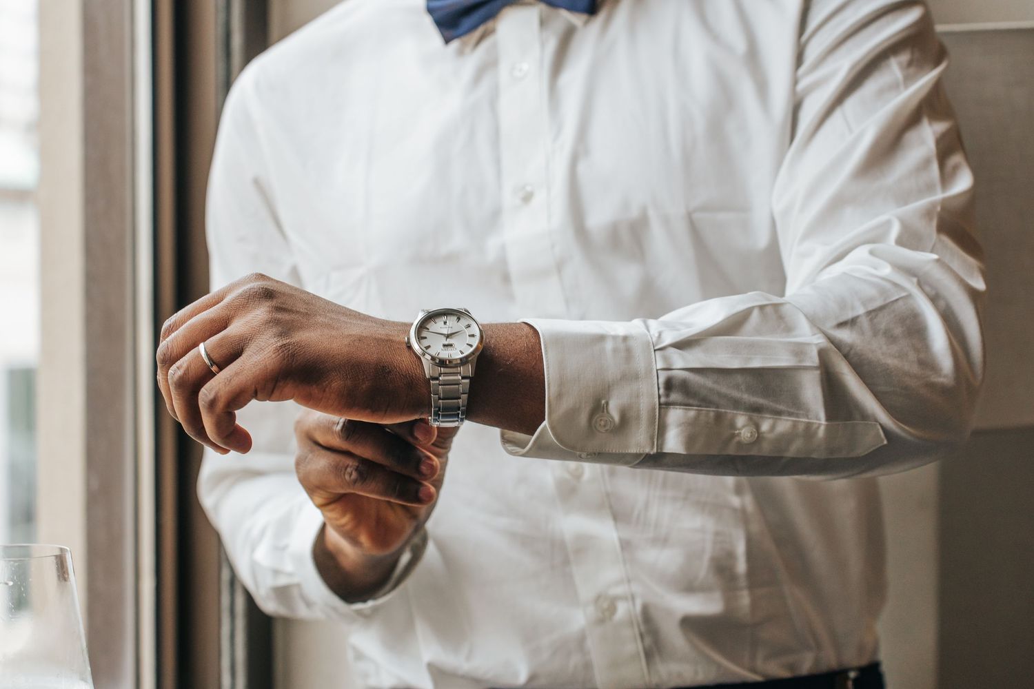 Close-up view of hands adjusting a blue bowtie on a white dress shirt.