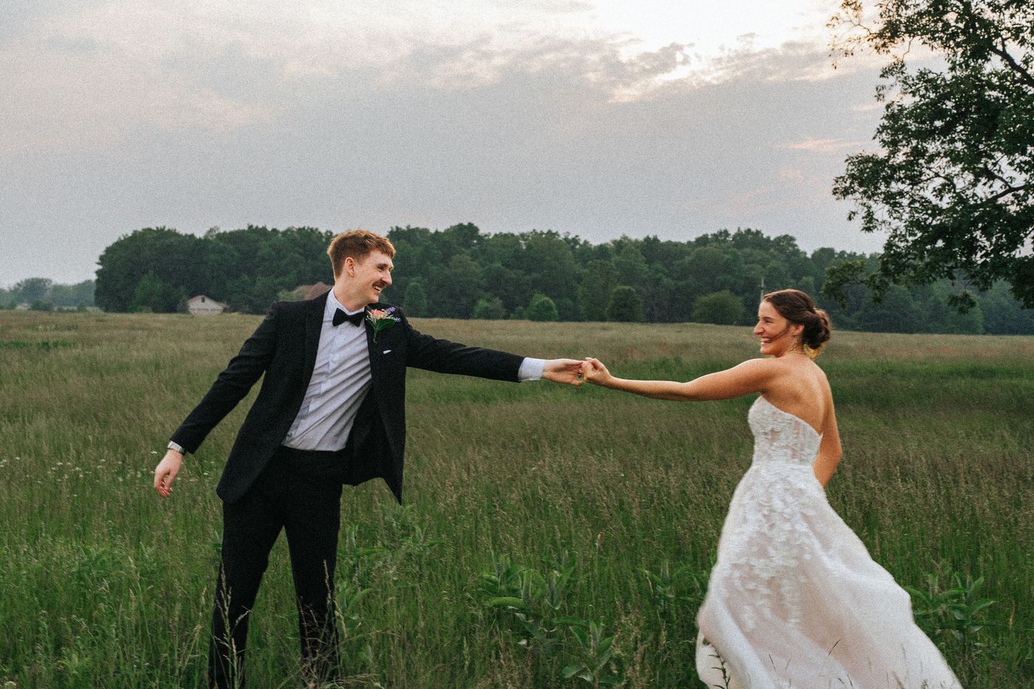 A couple in wedding attire playfully poses in a green meadow on their special day.