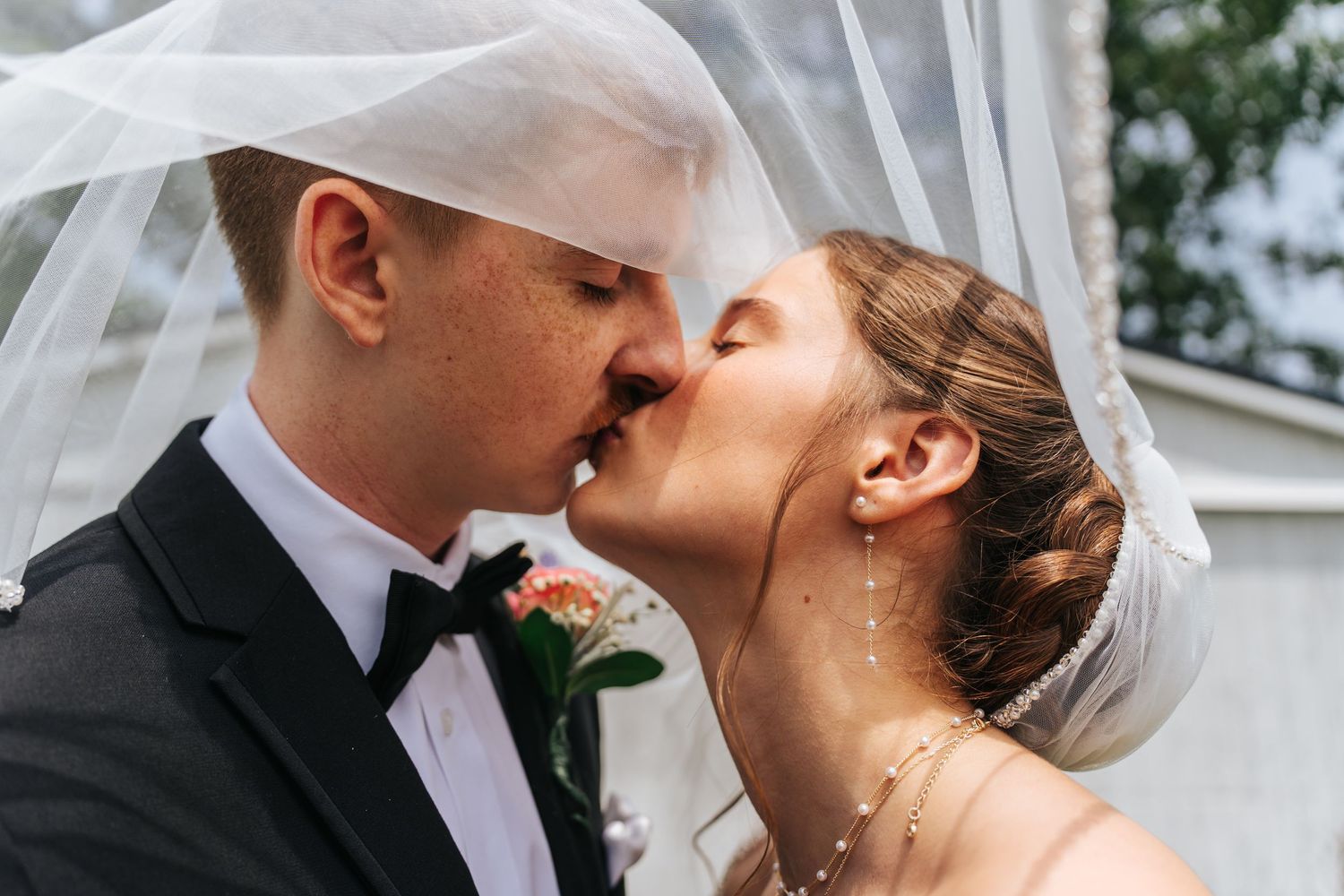 A romantic wedding couple shares an intimate kiss outdoors during their special day.