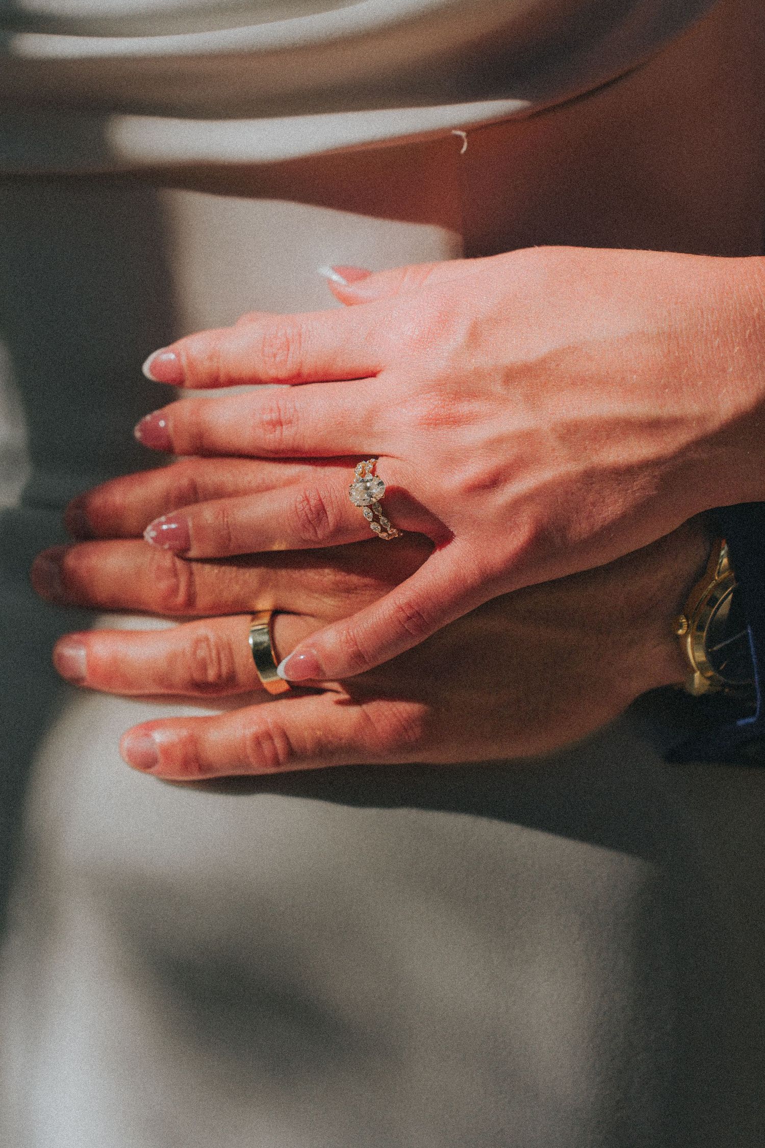 Two hands overlapping showing wedding rings, a diamond engagement ring and a gold band, symbolizing marriage and commitment.