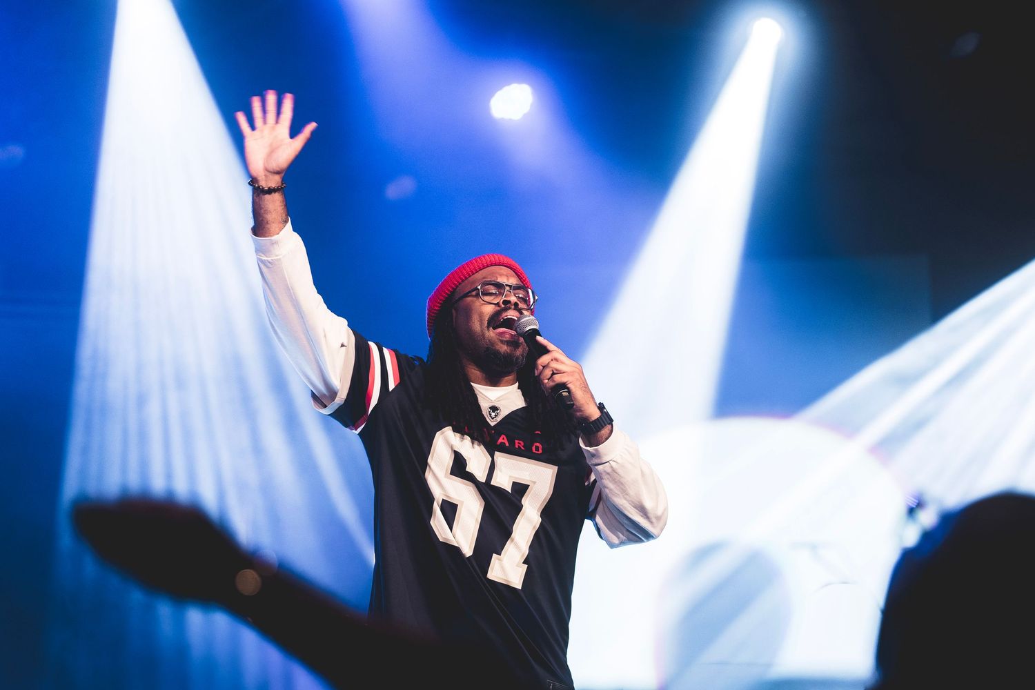 A performer on stage with raised arms sings passionately under dramatic blue concert lighting and spotlights.
