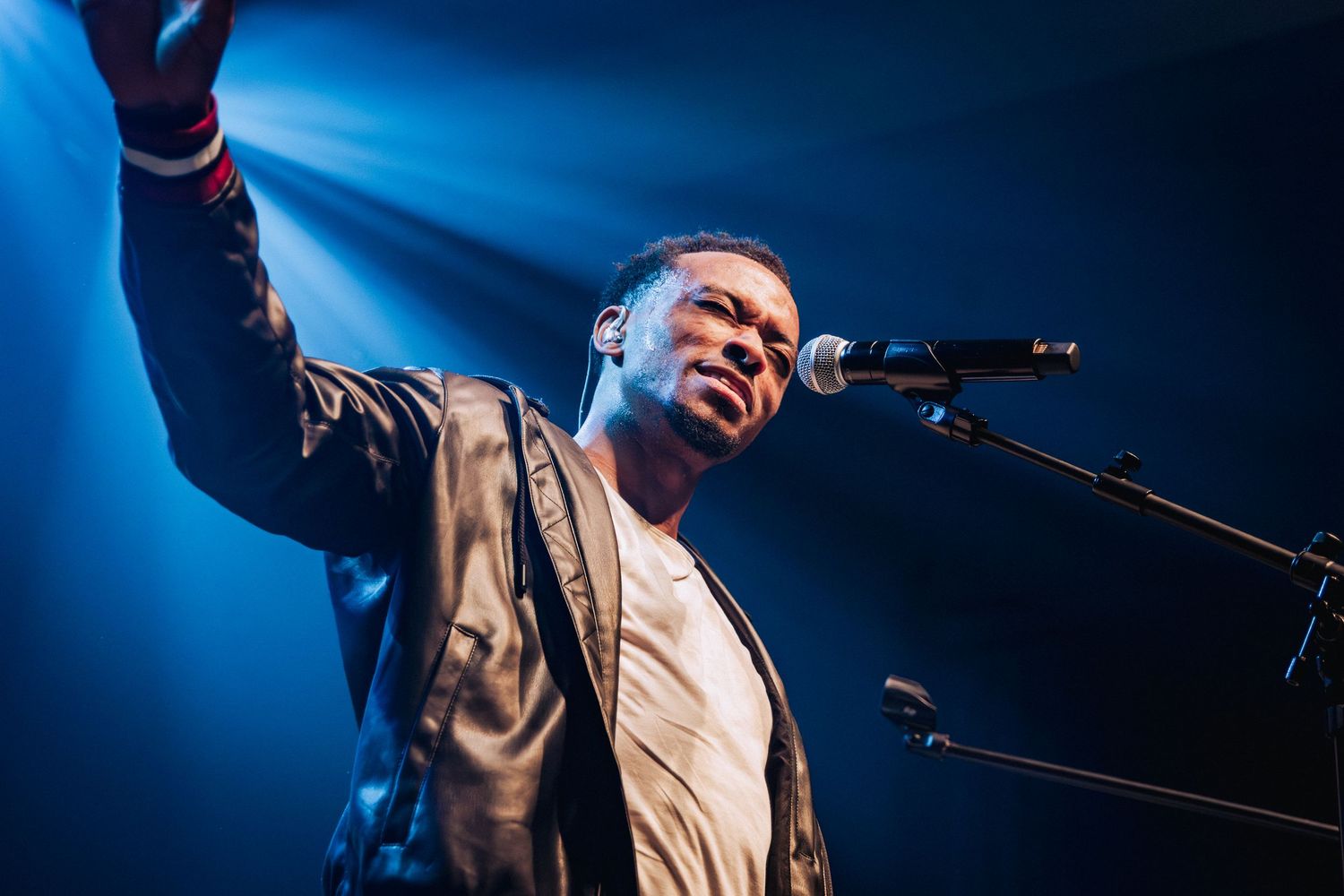 Artist performing energetically on stage with blue concert lighting.