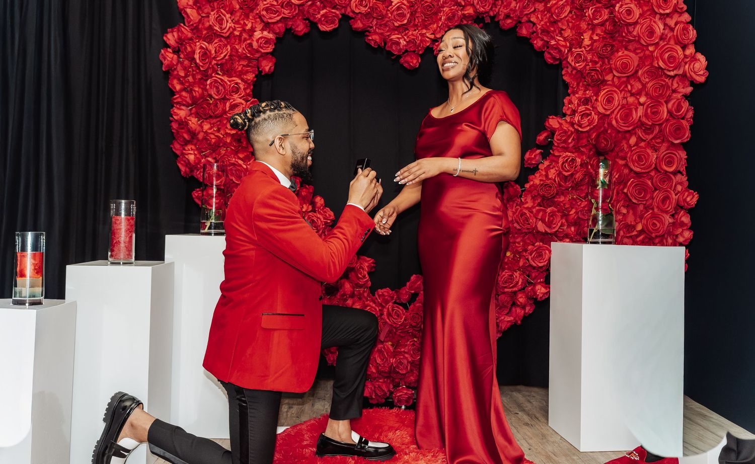 A romantic proposal scene unfolds against a backdrop of vibrant red roses as a couple shares an intimate moment.