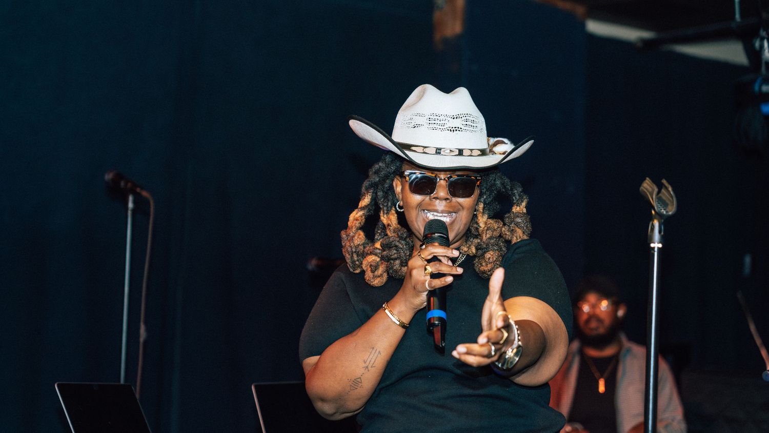 Performers on stage wearing cowboy hats during a dimly lit concert.