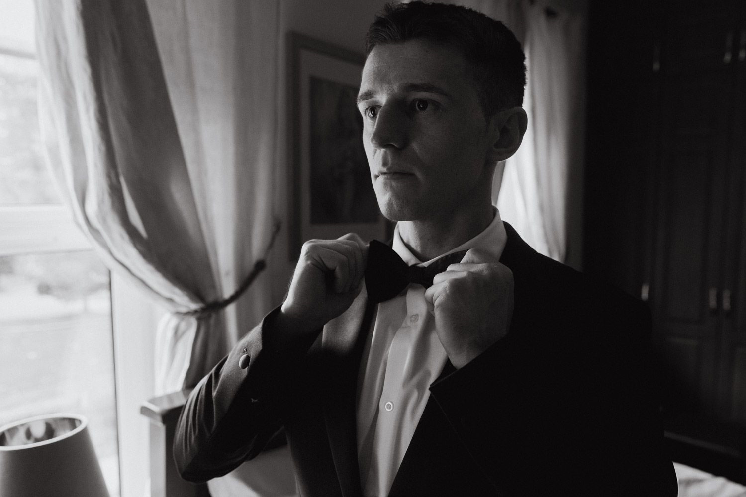 Black and white shot of Groom adjusting his bow tie during wedding morning preparations in Dublin