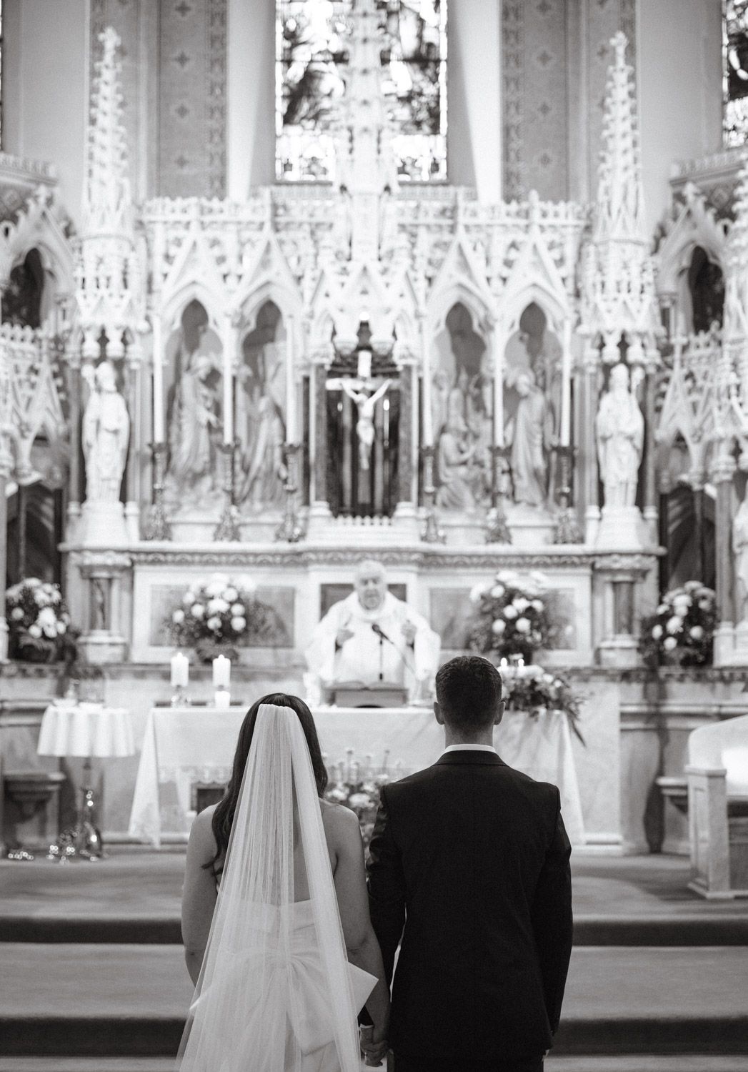 Black and white shot of bride and groom sitting holding hands at the altar in a classic church wedding in Dublin