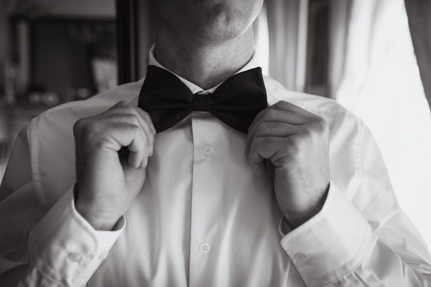 Groom adjusting his bow tie during wedding morning preparations