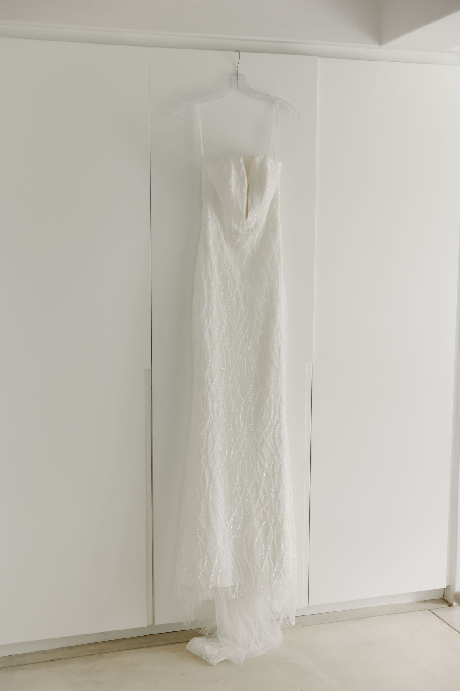Elegant white strapless wedding gown with lace details hanging on a hanger against white wardrobe doors.