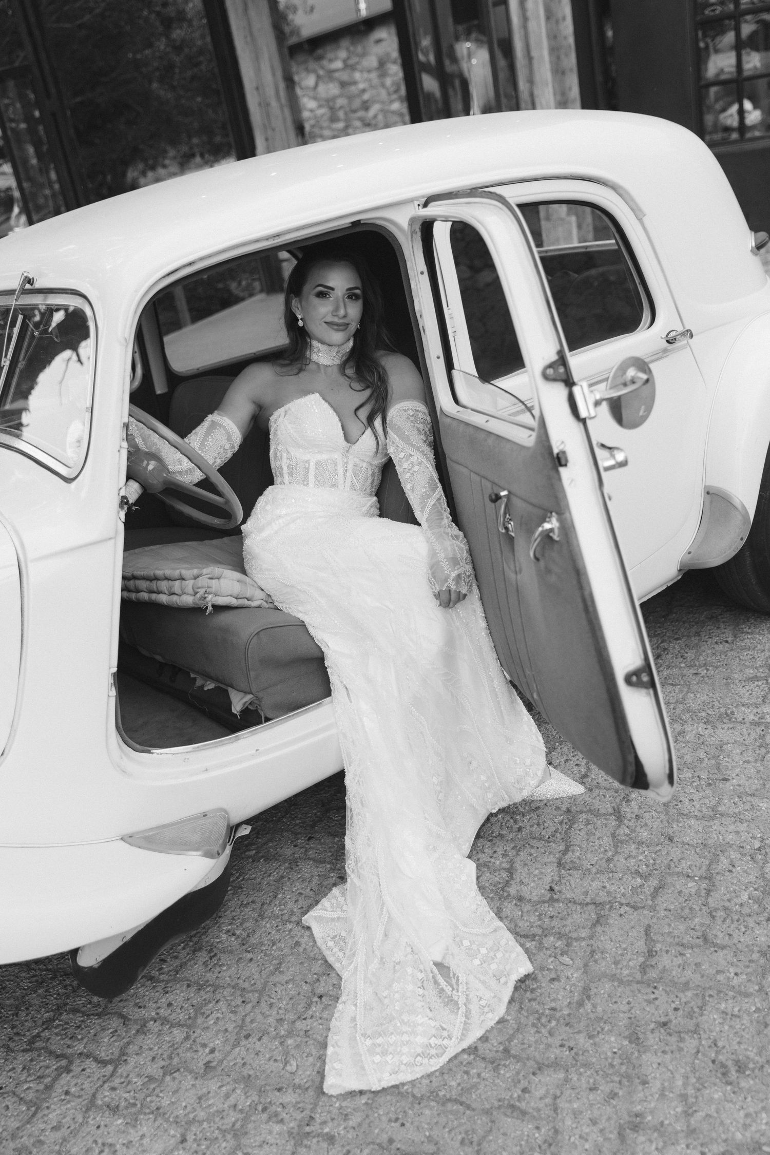 A bride in a white wedding dress gets into a vintage car in a series of black and white photos.