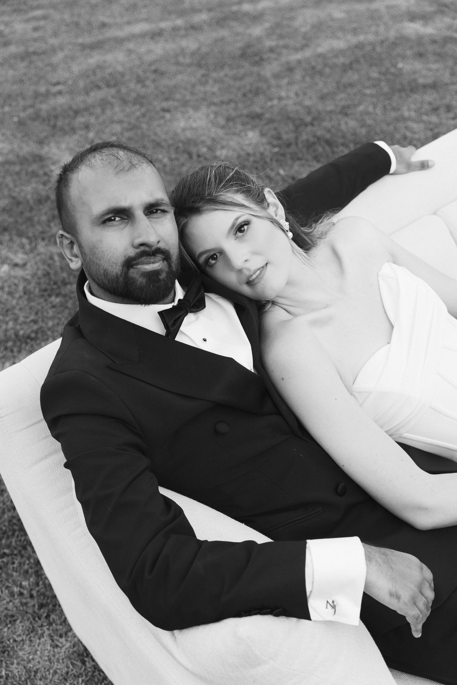 Black and white portrait of newlyweds lying together on grass.