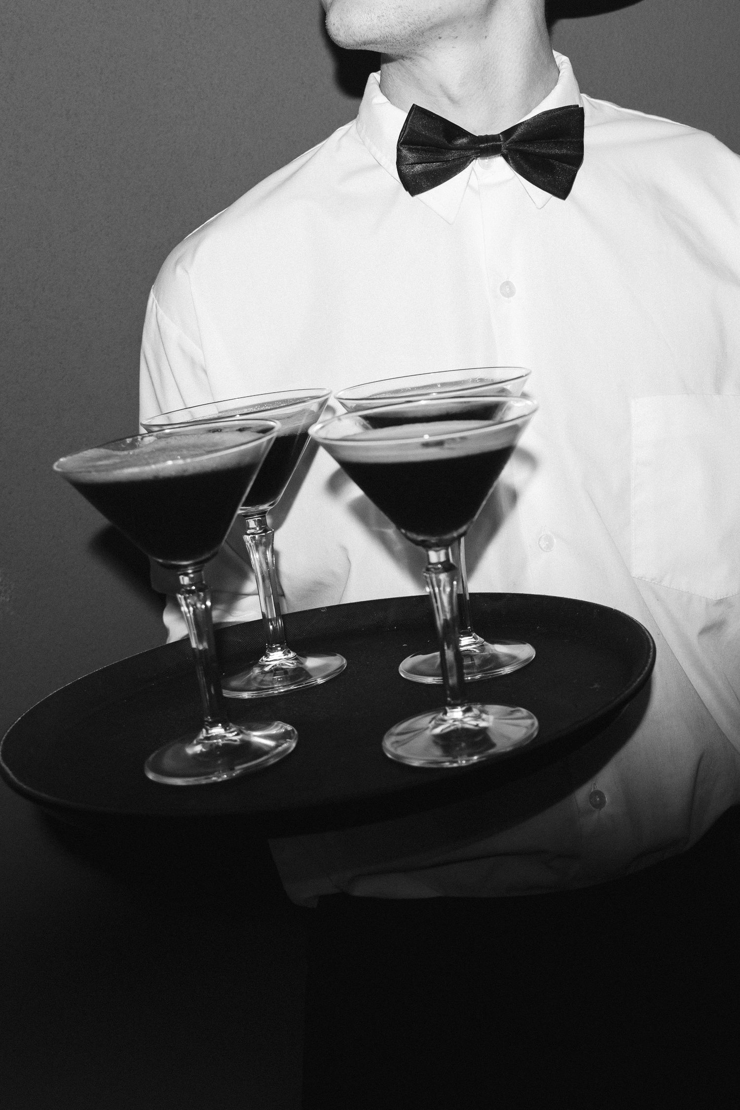 Black and white image of vintage champagne coupes arranged on a dark serving tray with bow tie service detail.