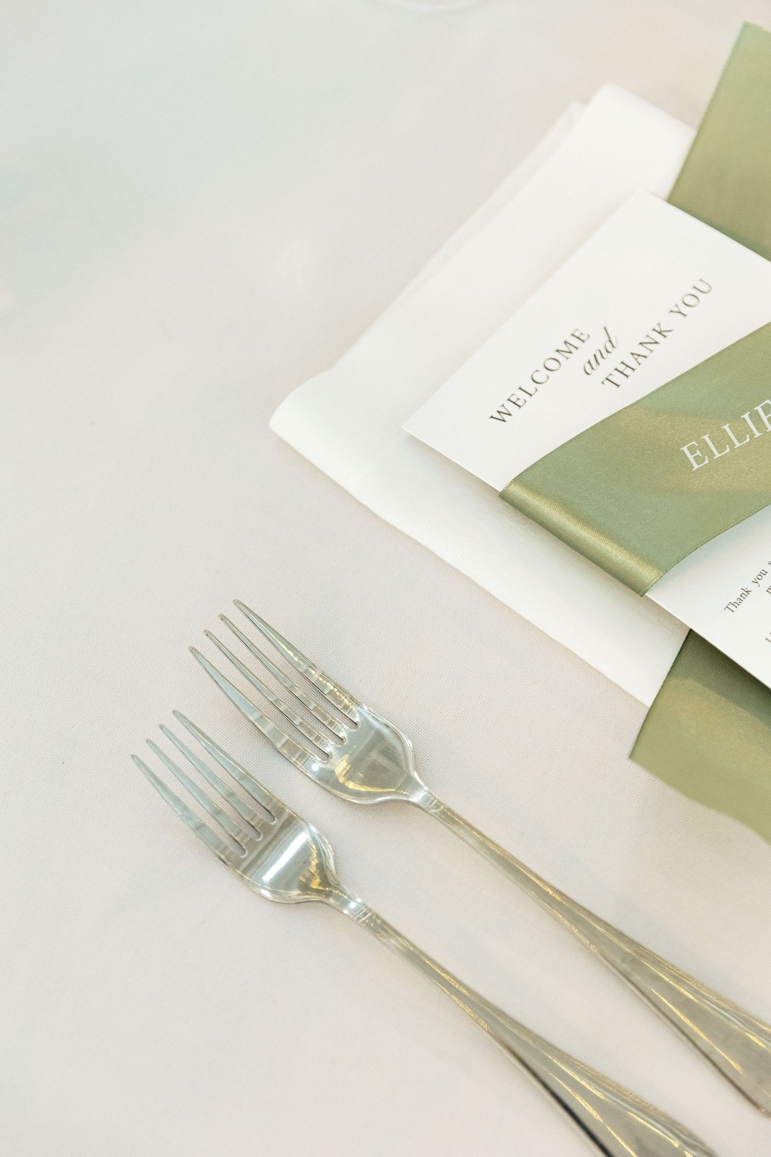 Elegant place setting with silverware and white napkin against soft green background in modern minimalist style.