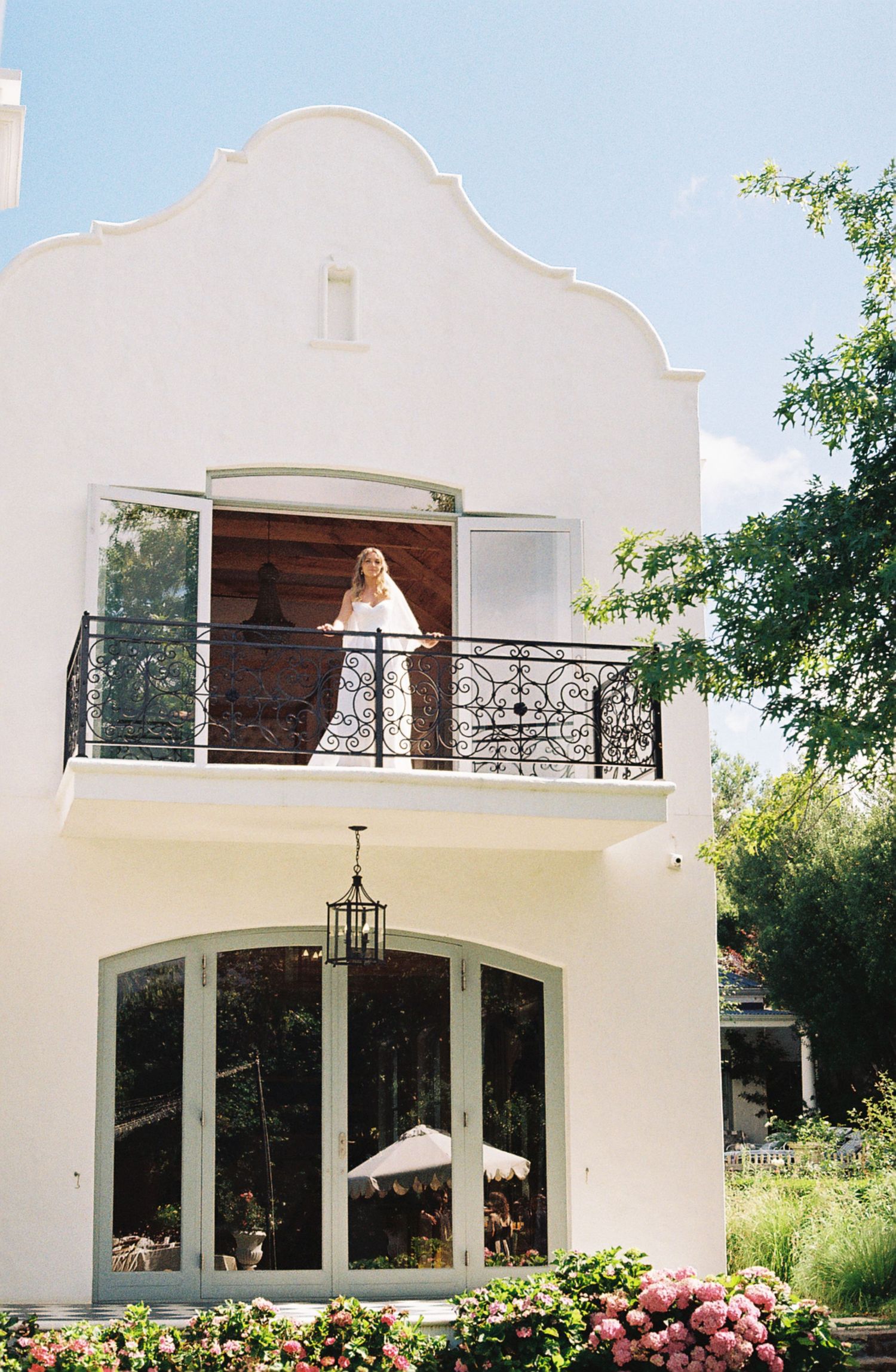 Elegant white Mediterranean-style villa with arched windows and balconies adorned with pink flowering bushes.