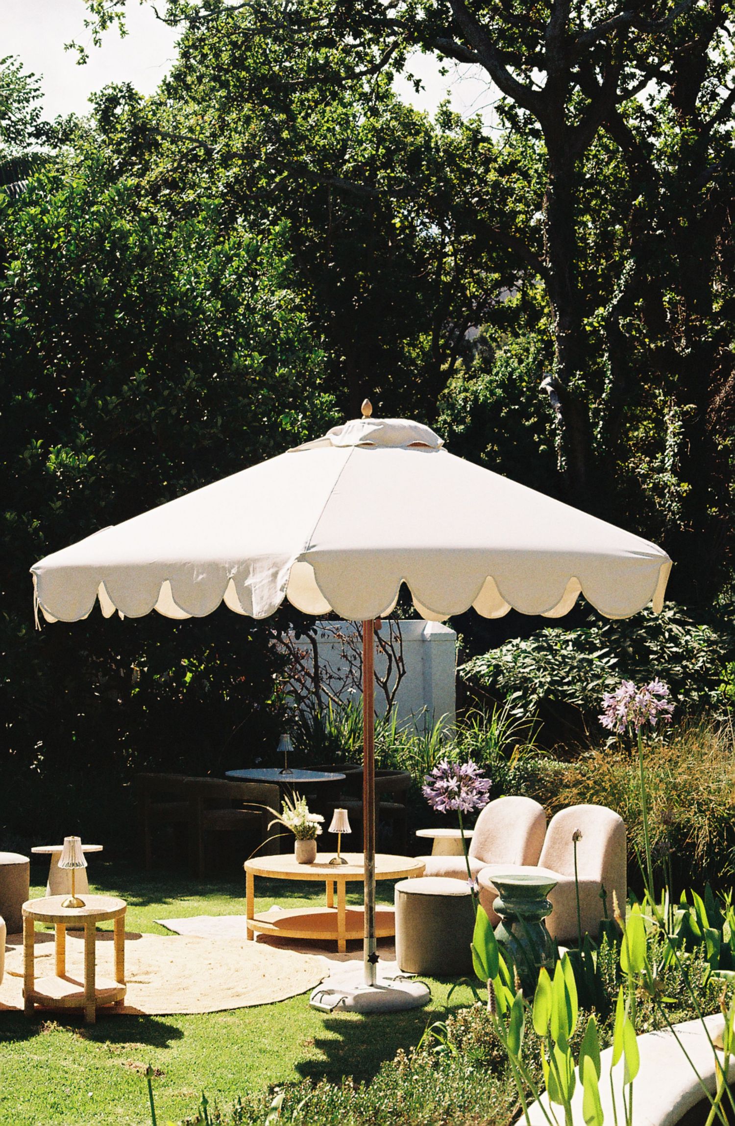 Outdoor garden seating area with white umbrella parasols and wooden furniture arranged on a patio surrounded by greenery.