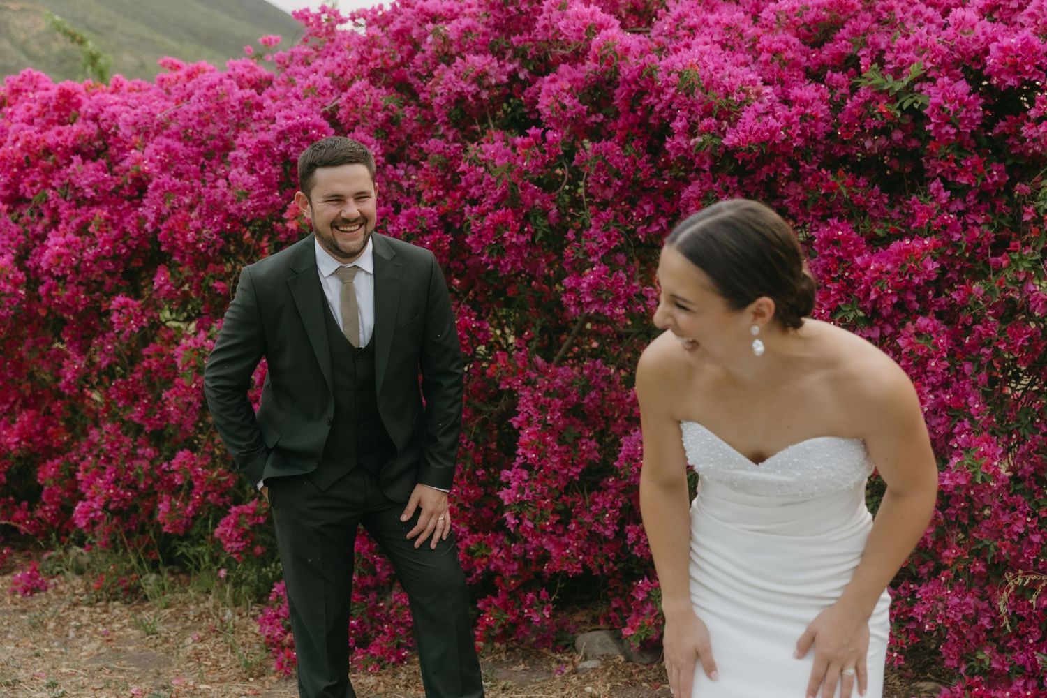 A wedding couple poses in front of vibrant pink azalea bushes during their spring celebration.