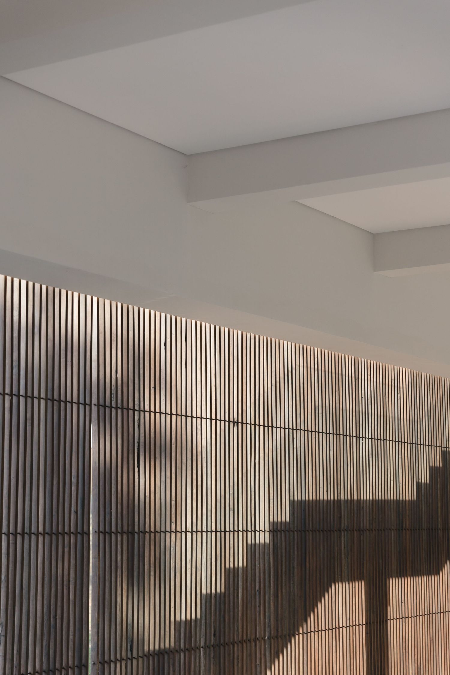Minimalist art installation shows vertical metal bars casting dramatic diagonal shadows on a white gallery wall.