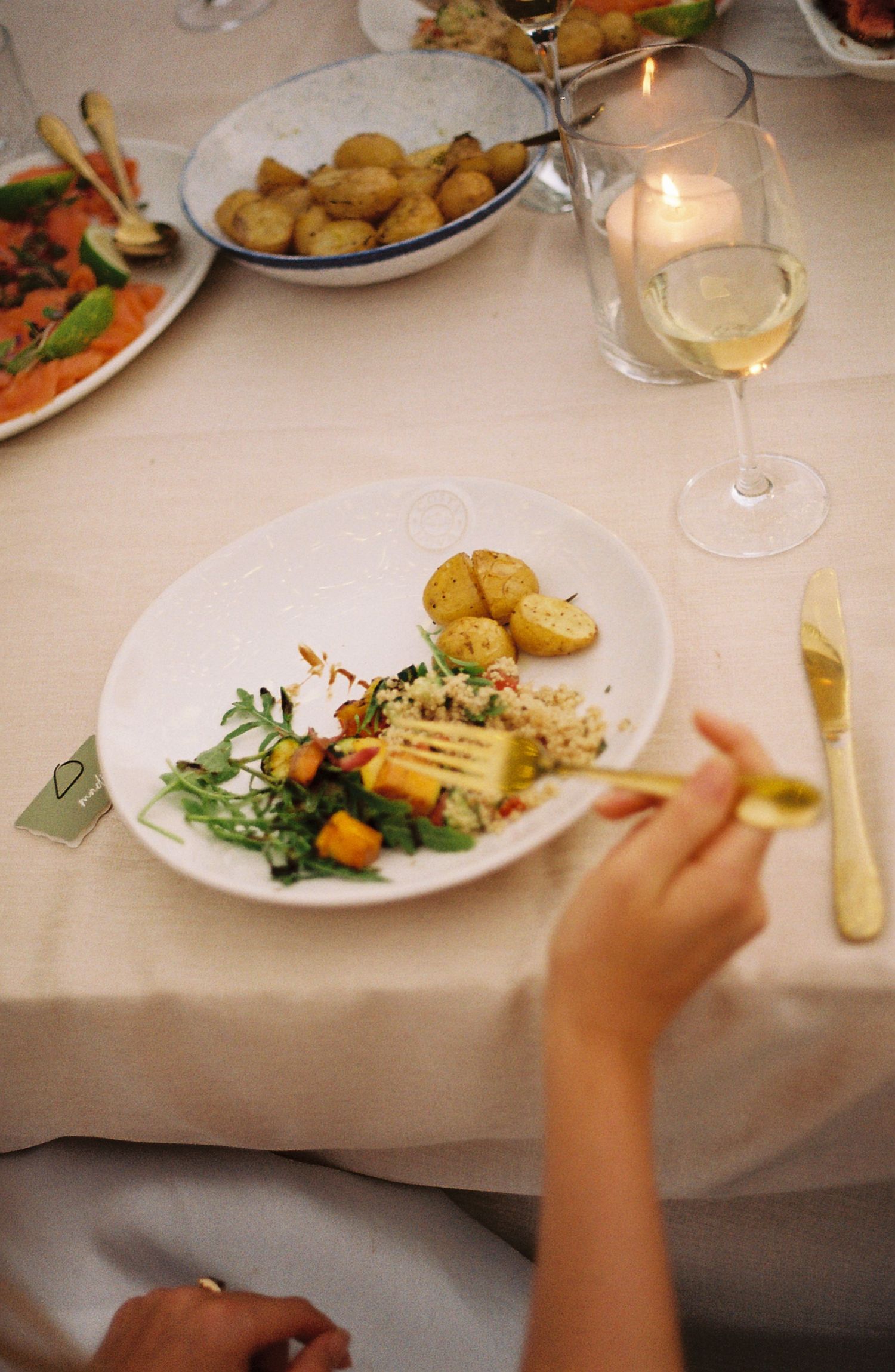 Hands reaching for elegant plated dishes at a formal dinner table with wine glasses and candles.