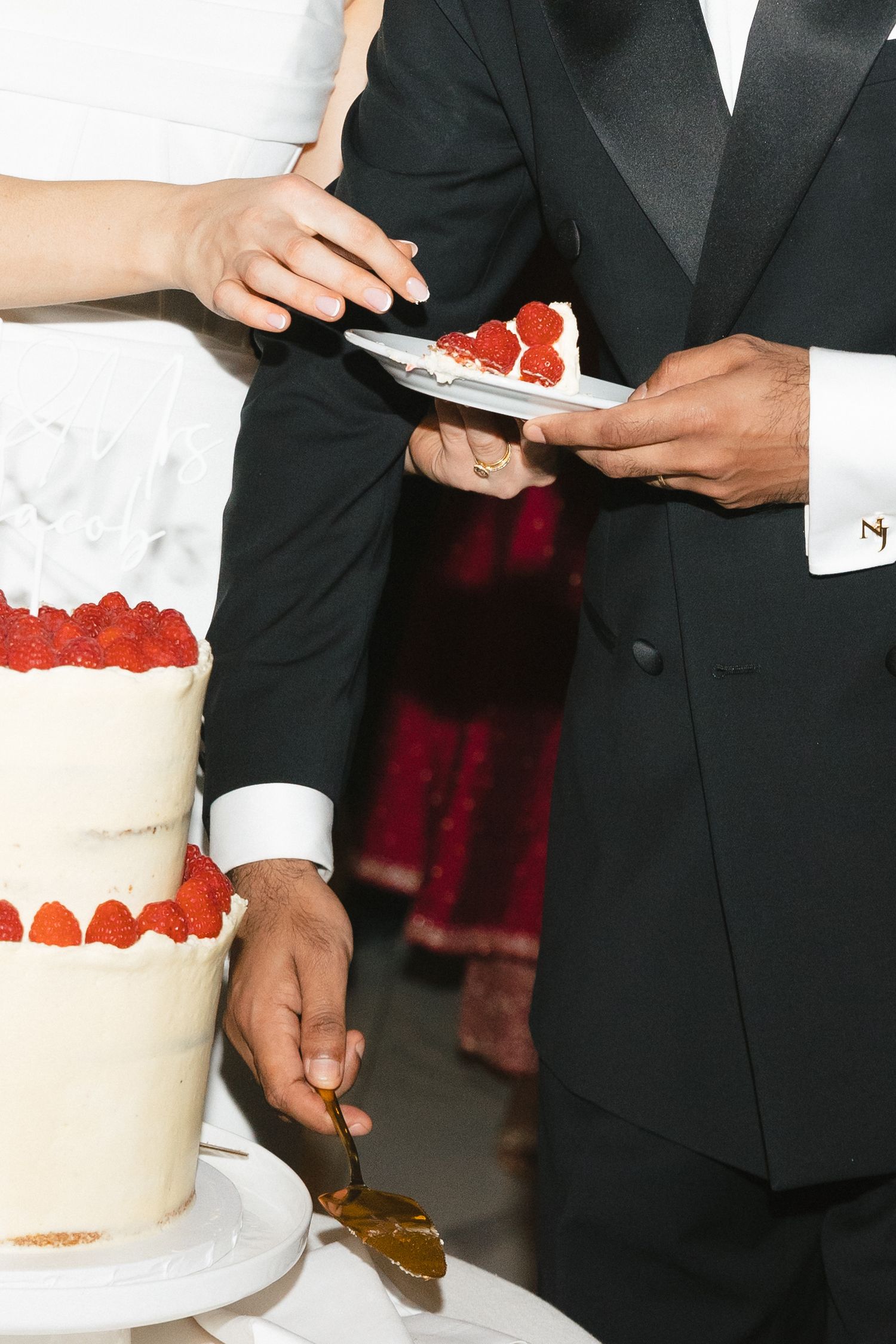 Close-up shots of hands cutting into a white wedding cake decorated with fresh red berries.
