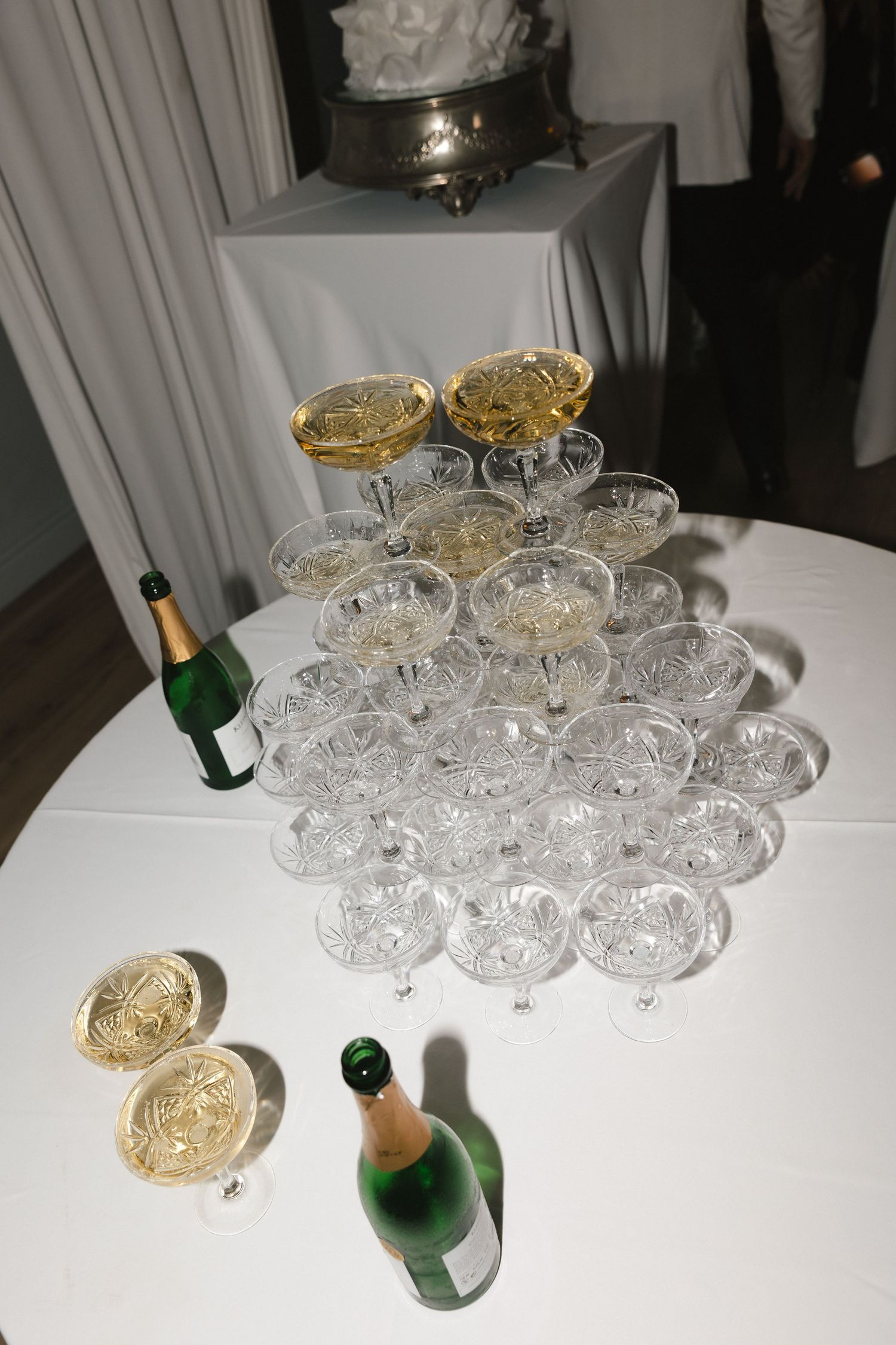 Crystal champagne coupes and wine glasses arranged on white tablecloth with gold accent pieces.