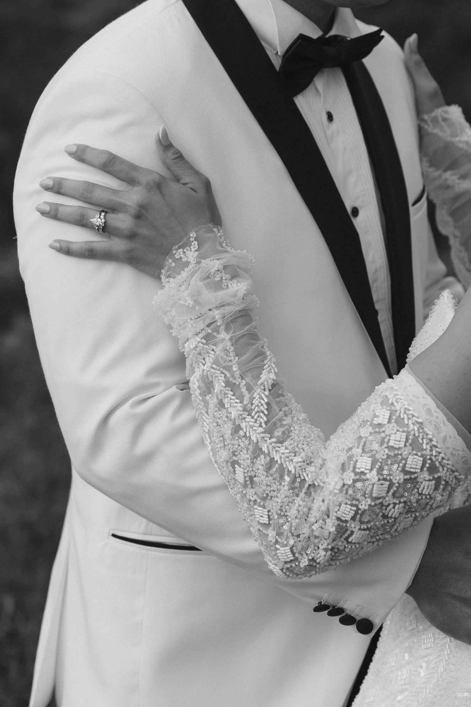 Close-up black and white photo showing intricate lace sleeve details on a formal white tuxedo jacket.
