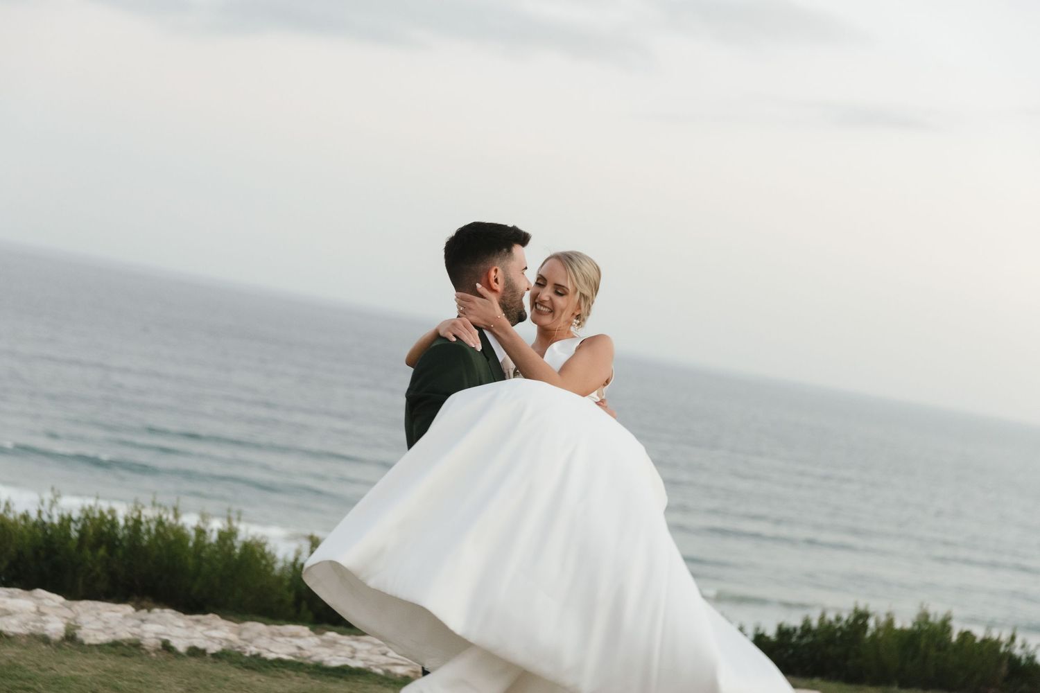 A romantic beach wedding scene with a couple embracing against an ocean backdrop in white wedding attire.