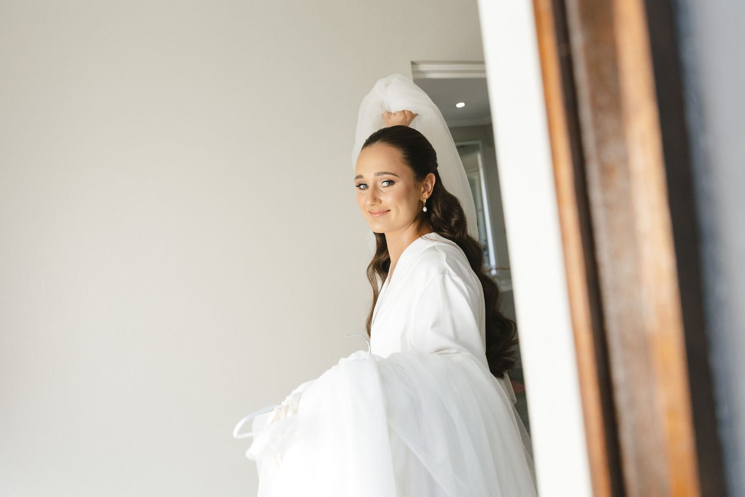 Person in a white robe stands in a minimalist interior hallway with natural lighting.