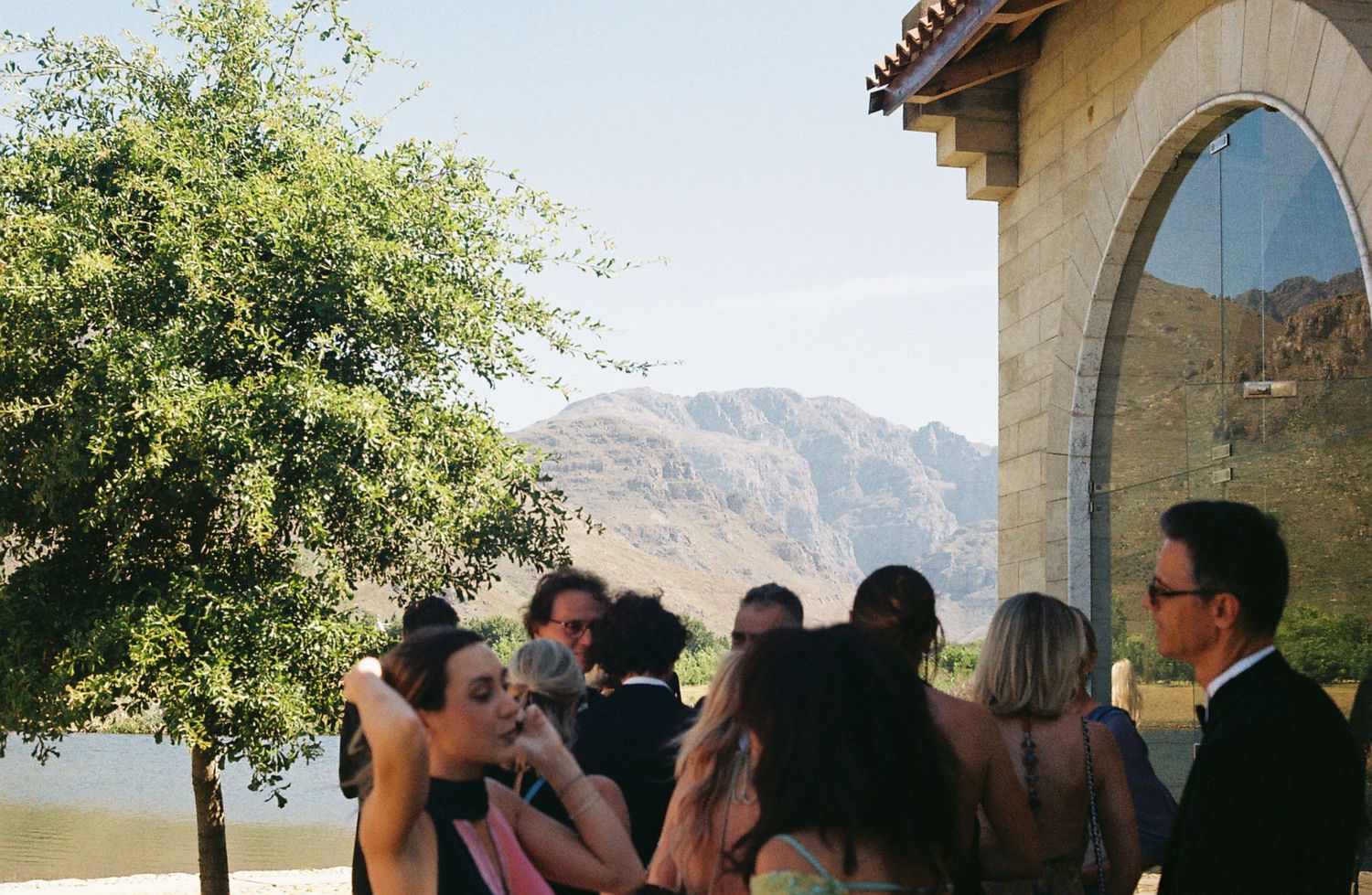 A panoramic view of a wedding ceremony taking place outdoors with mountains and trees in the background.