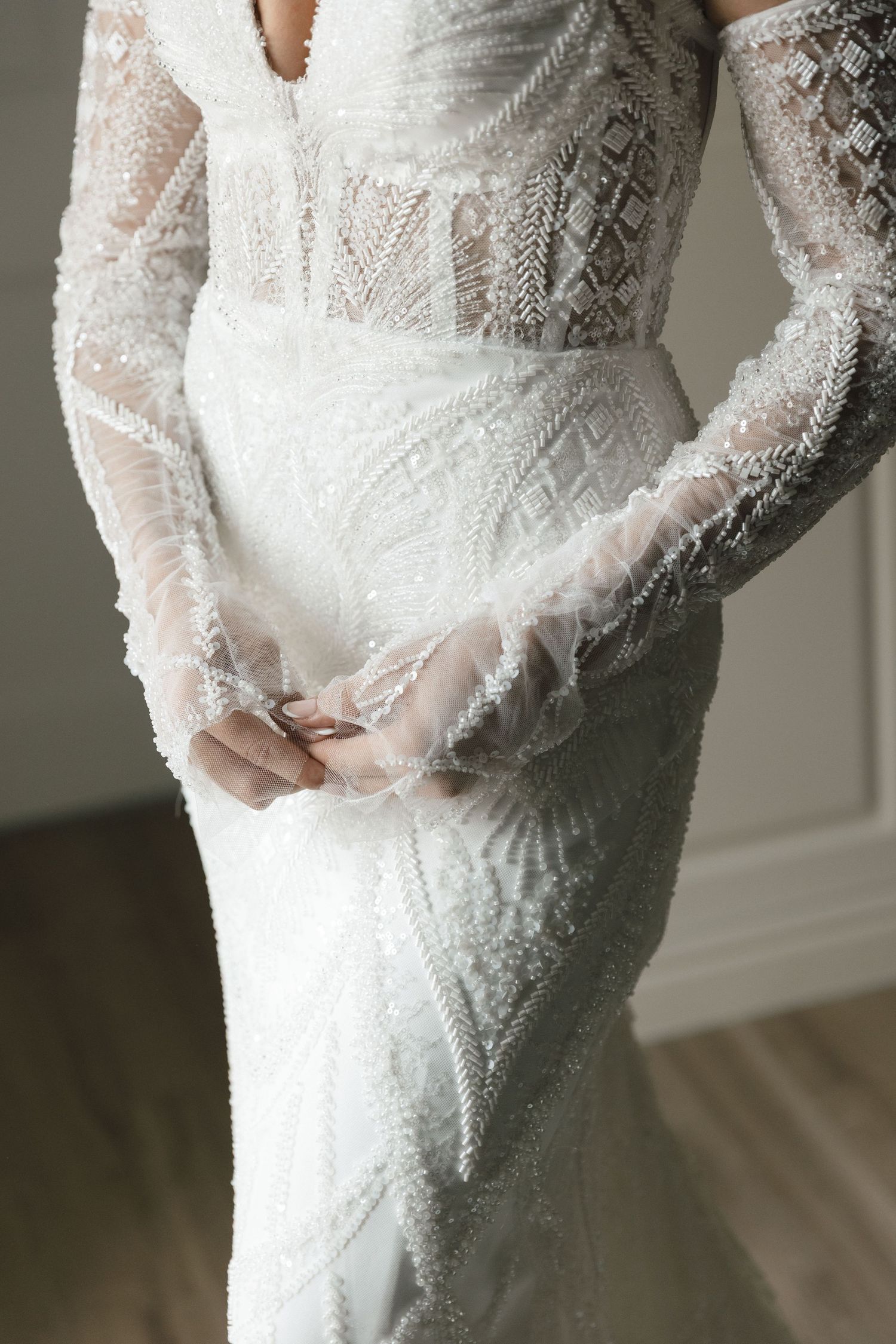Close-up details of an elegant white lace wedding dress with long sleeves and intricate beading patterns.